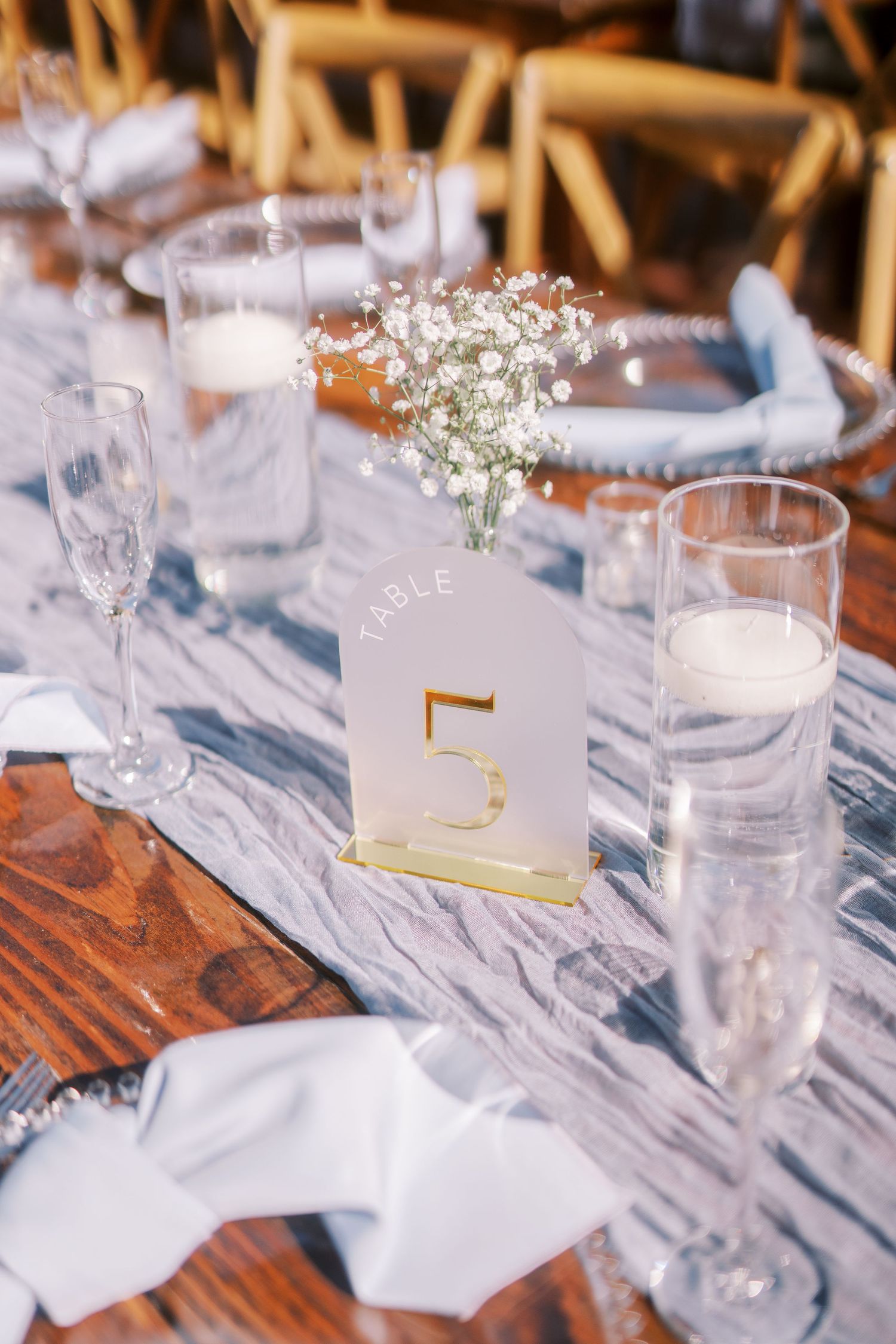 Elegant wedding table setting with white linen, champagne glasses, and baby's breath centerpiece with gold table number.