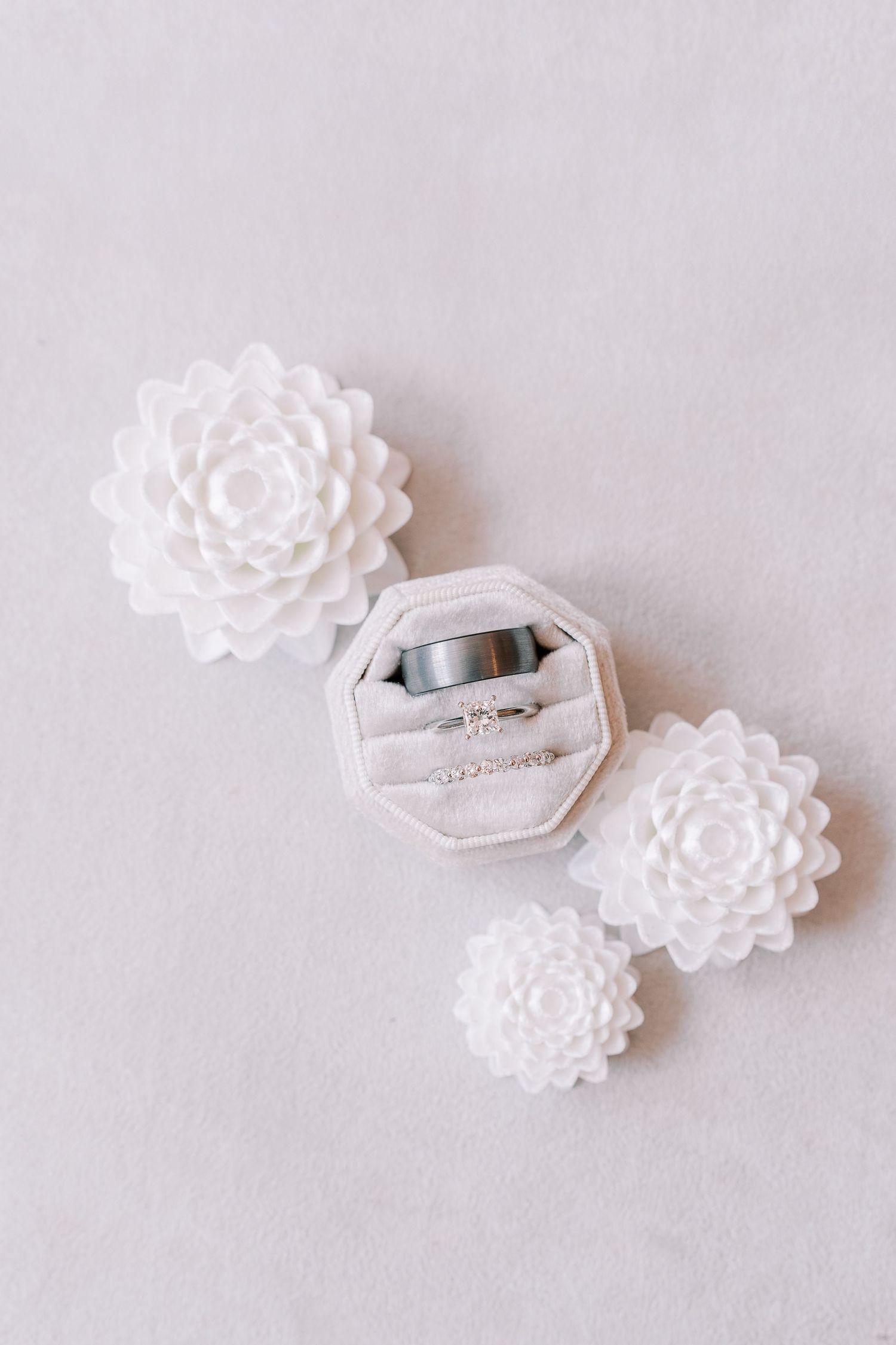 Wedding rings displayed in a white velvet octagonal ring box surrounded by delicate white floral decorations.