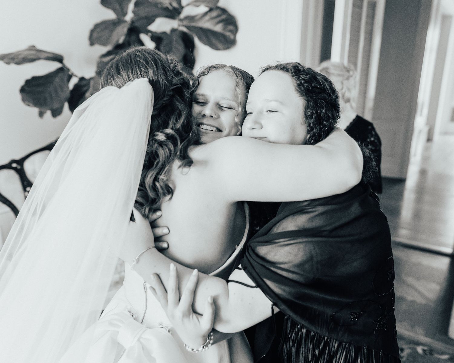 An emotional wedding moment captured in black and white as a bride embraces loved ones, sharing tears and smiles.