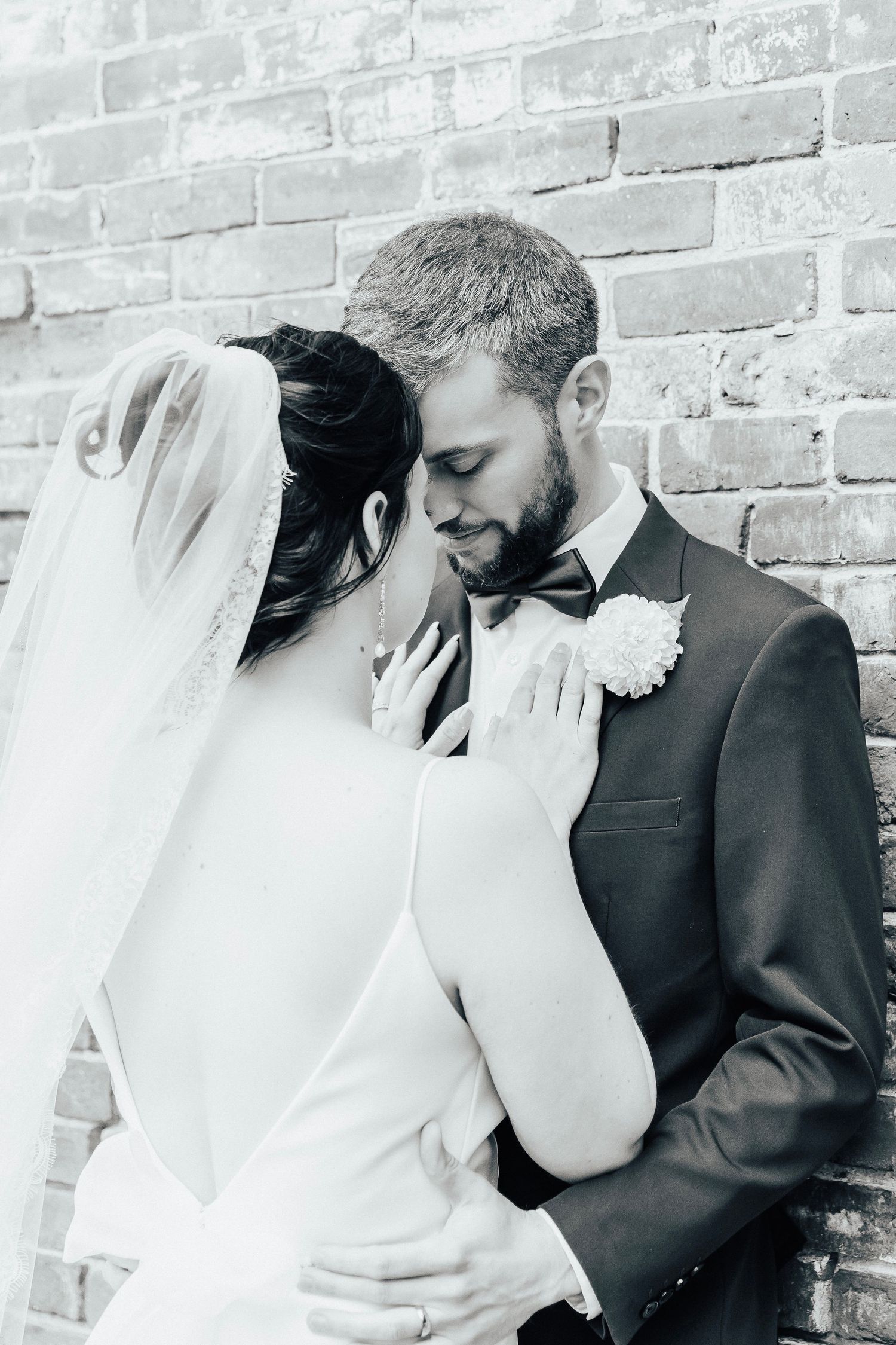 Black and white romantic wedding portrait against brick wall.