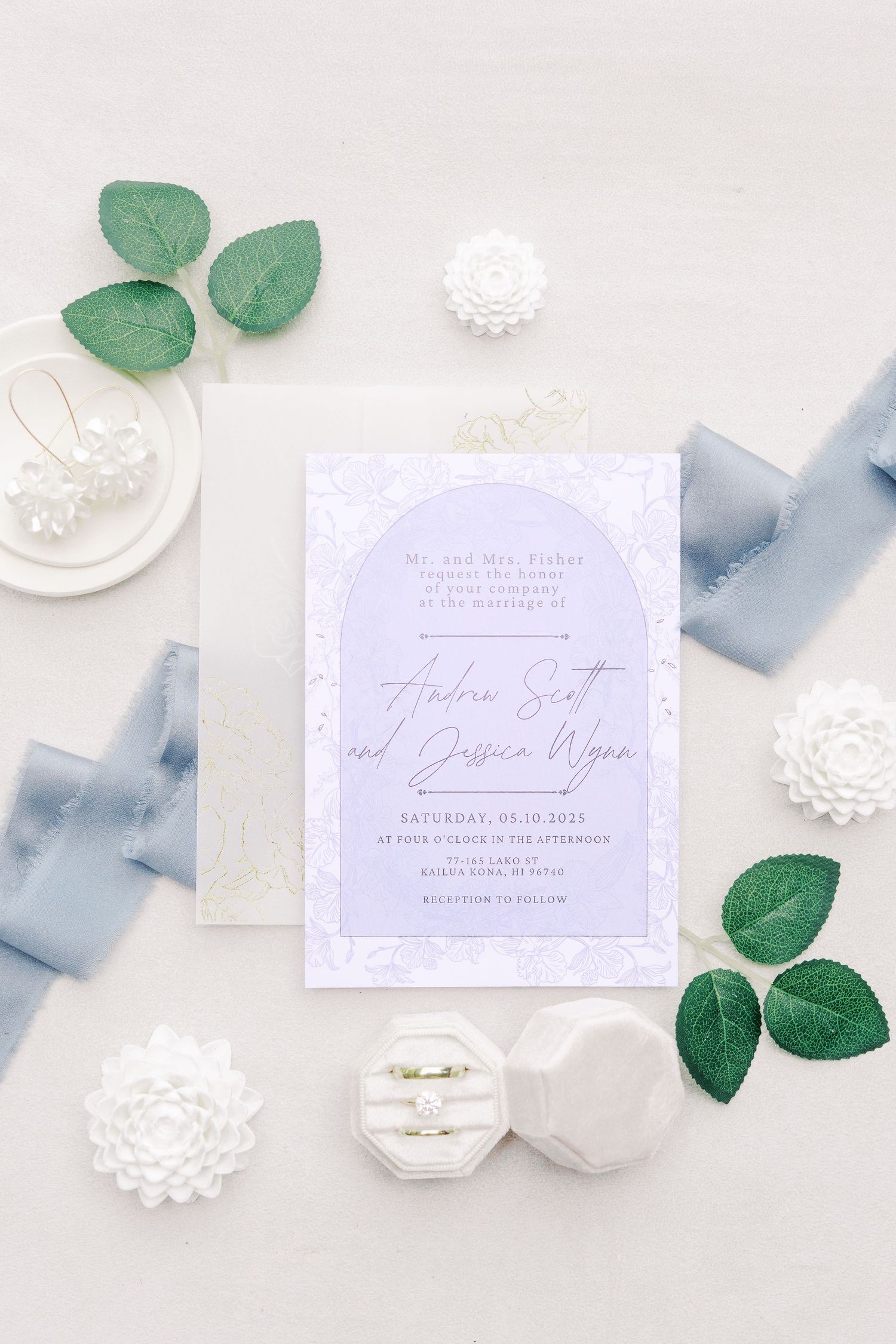 A sophisticated wedding invitation in light blue with greenery and white floral accents.