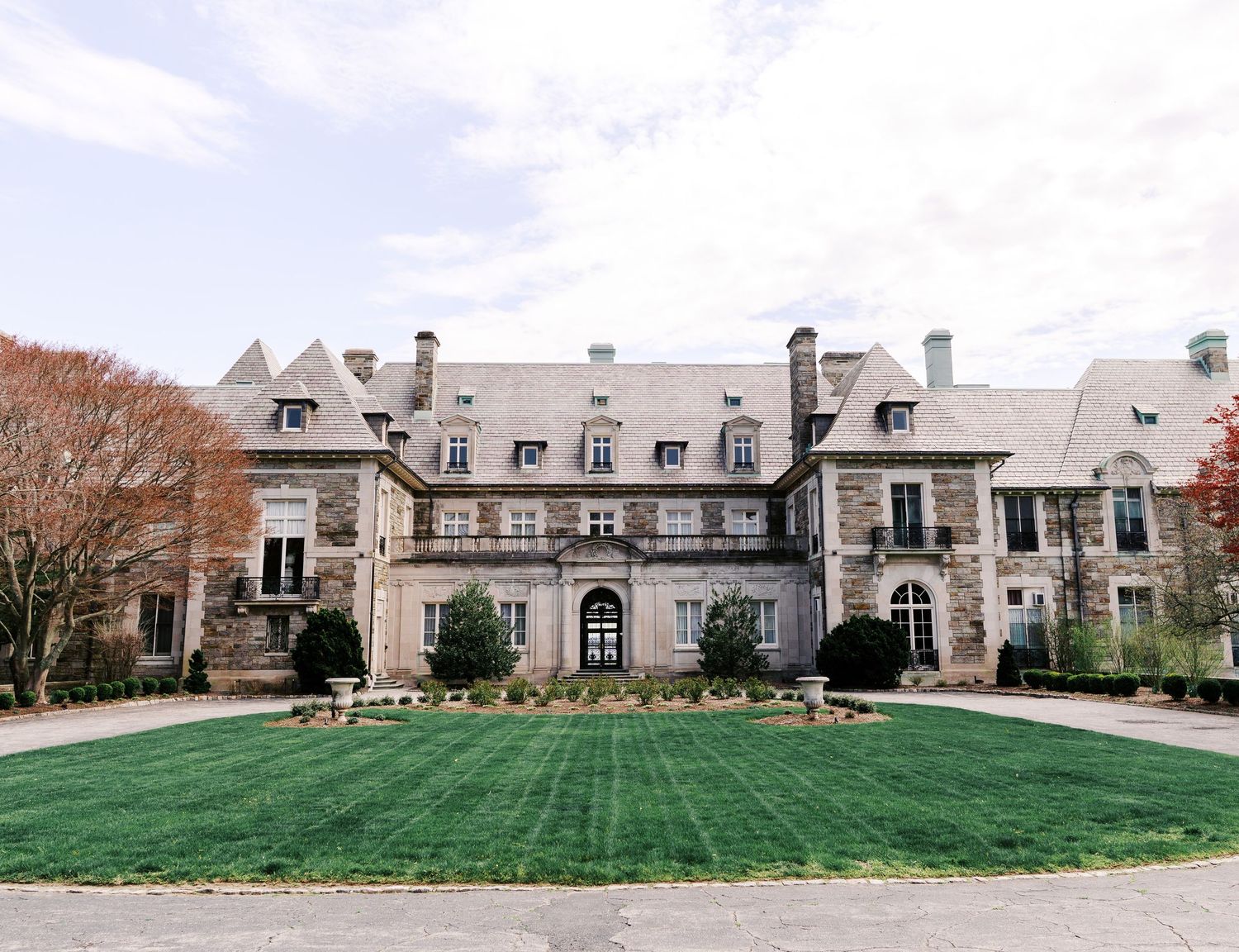 Elegant stone mansion with French-inspired architecture features dormered windows and a manicured green lawn courtyard.