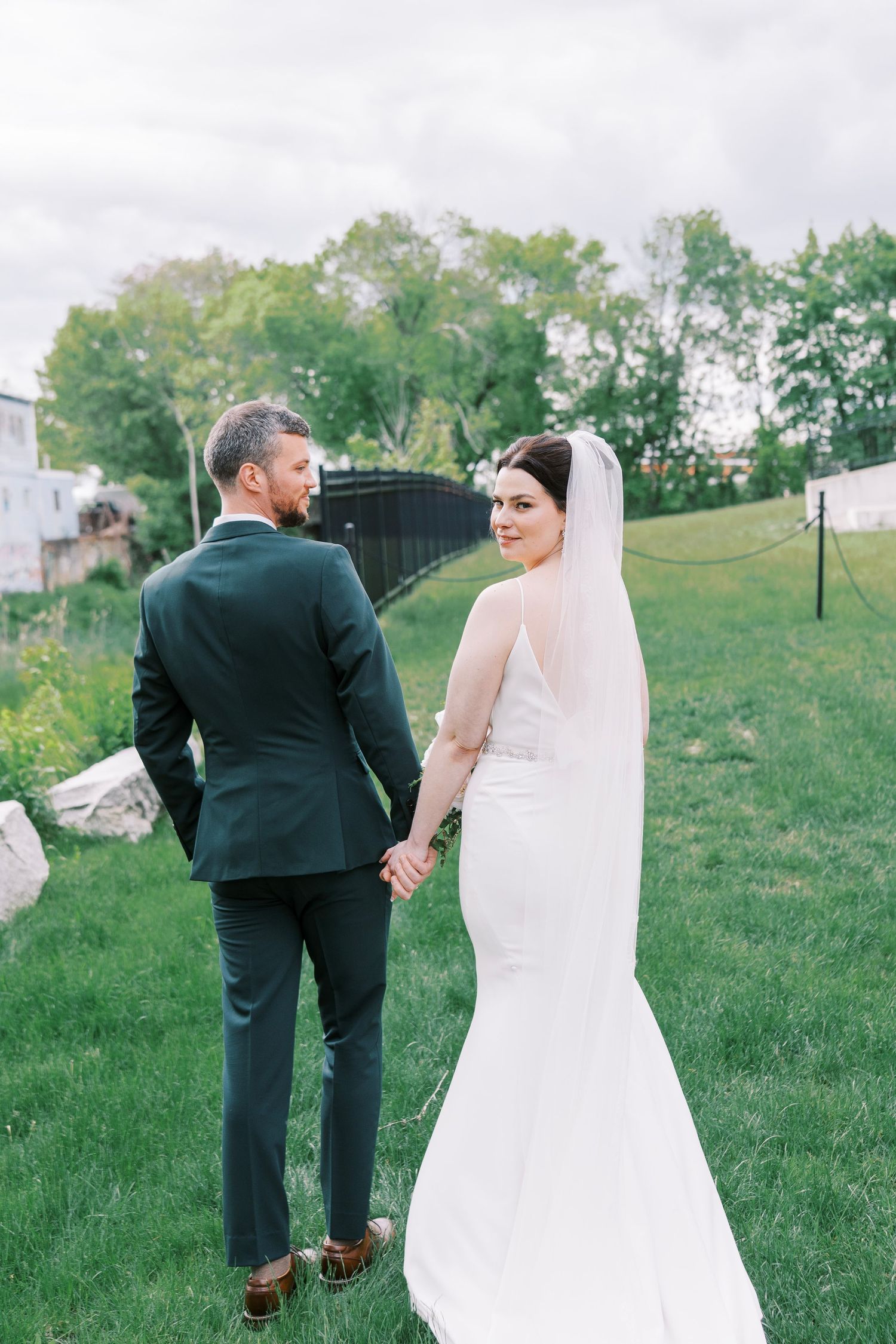 Bride and groom hold hands in a romantic outdoor garden setting.