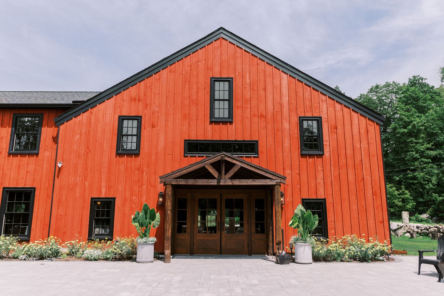 Four matching red barn-style event venues with rustic wooden beams and glass windows set against a cloudy sky.