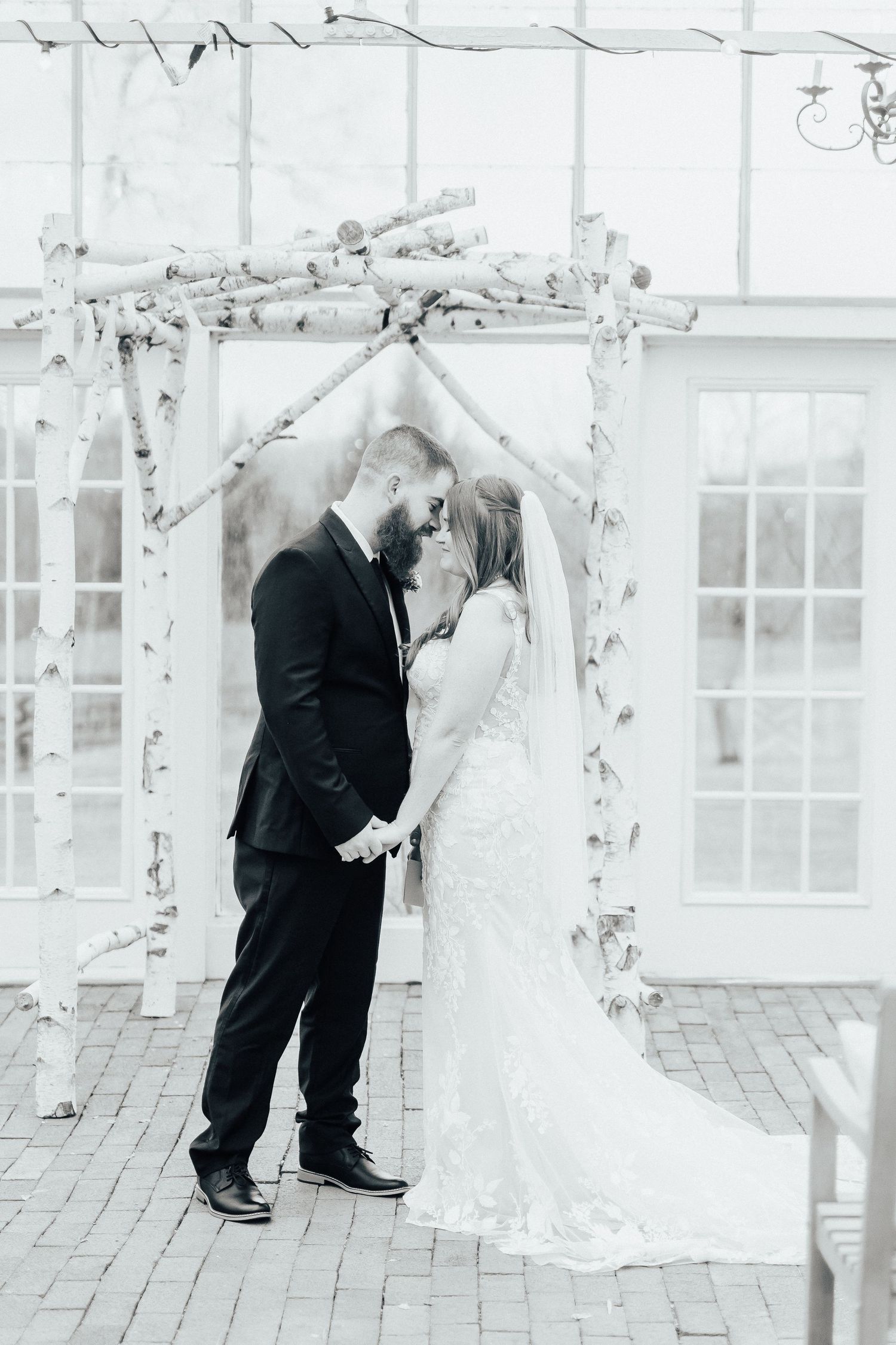 Black and white photo of a couple sharing their first kiss under a birch branch wedding arch.