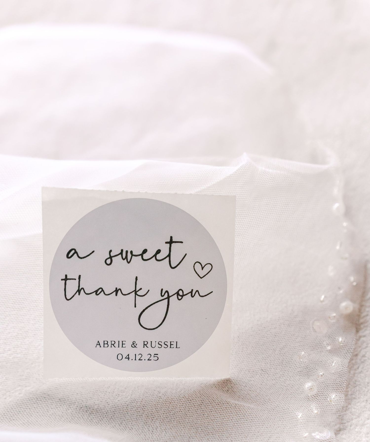 Minimalist thank you sticker with handwritten text and wedding date on white fabric background.