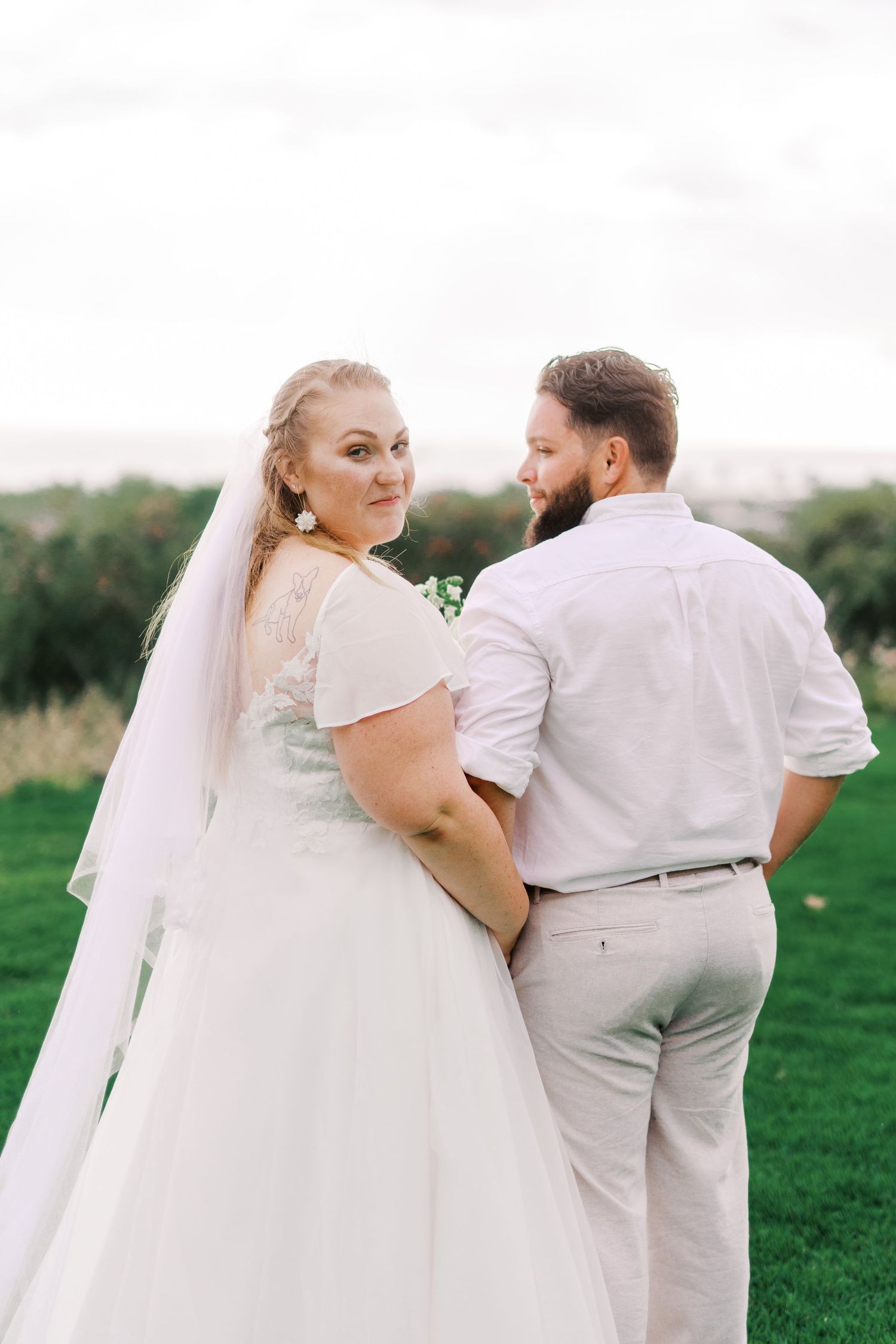 Romantic wedding photos of a couple in white attire walking together on green grass.