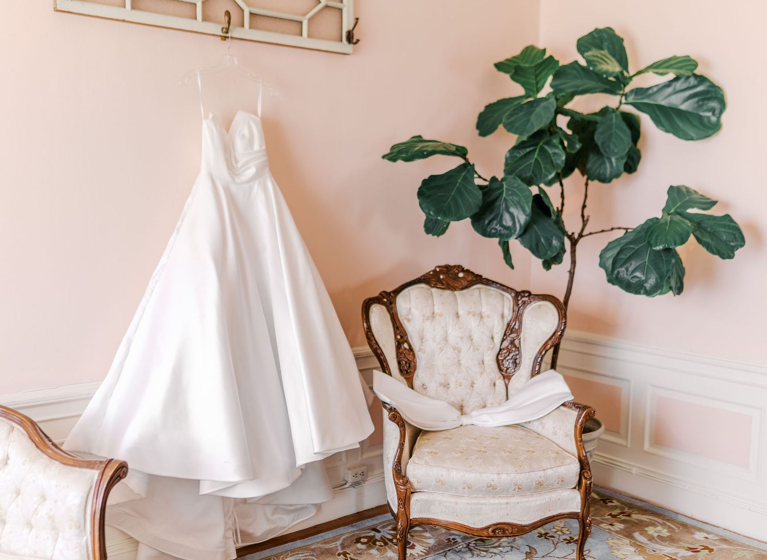 Delicate bridal gowns in white displayed on dress forms with vintage furnishings and green foliage accents.