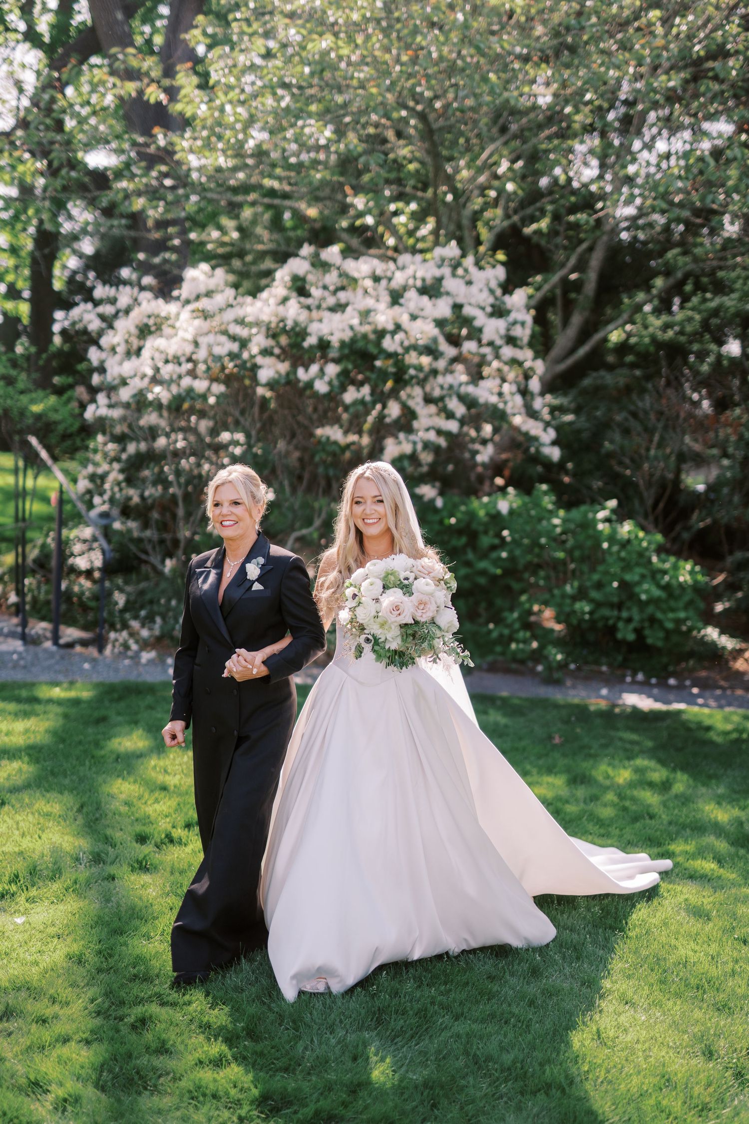 A bride in a romantic garden setting walking on a grassy lawn surrounded by blooming spring trees.