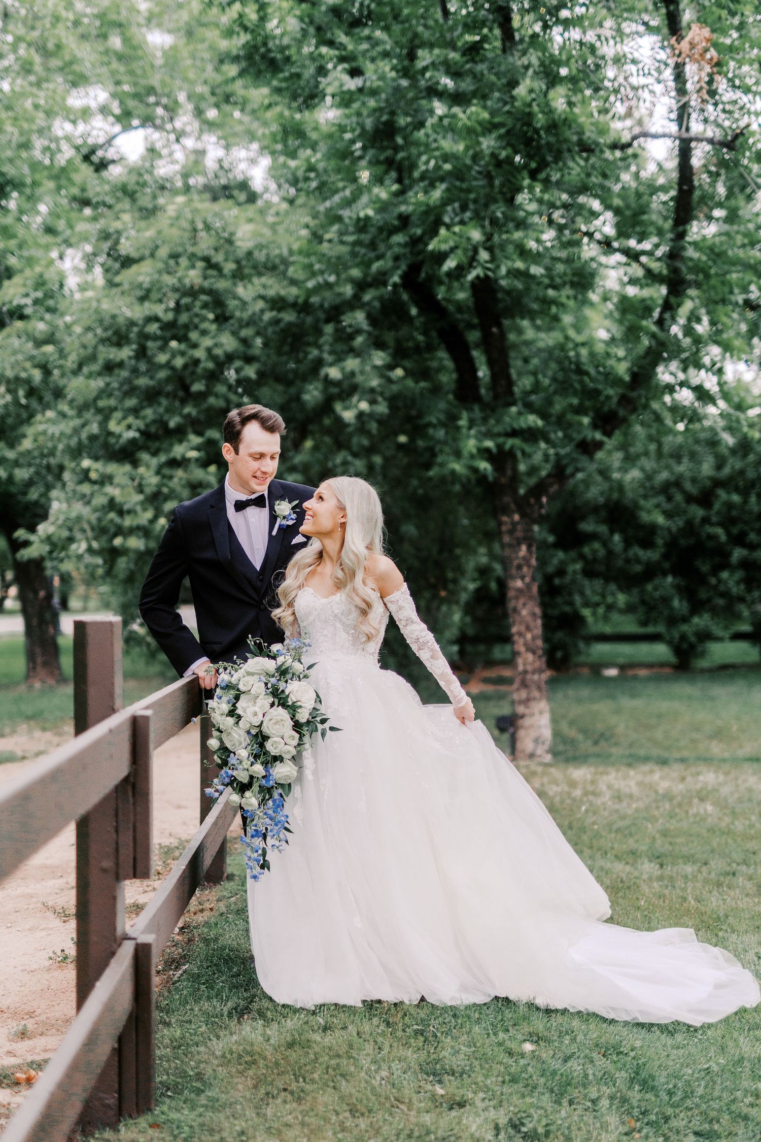 A couple poses together on a rustic wooden bridge surrounded by lush green trees on their wedding day.