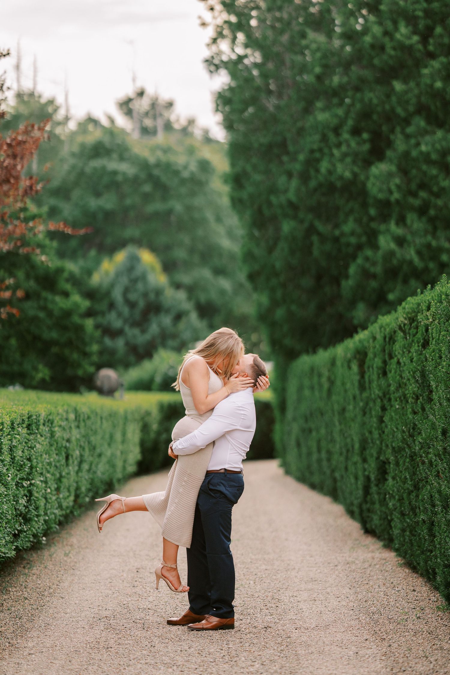 Romantic couple embracing on garden pathway surrounded by green hedges.