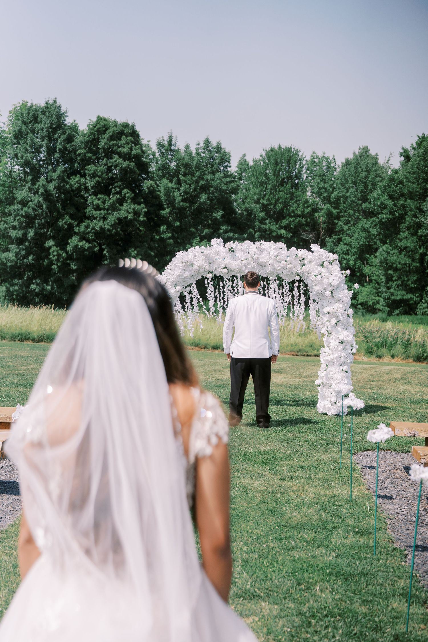 A sequence of wedding ceremony moments at an outdoor garden venue with a white floral arch and green trees in background.