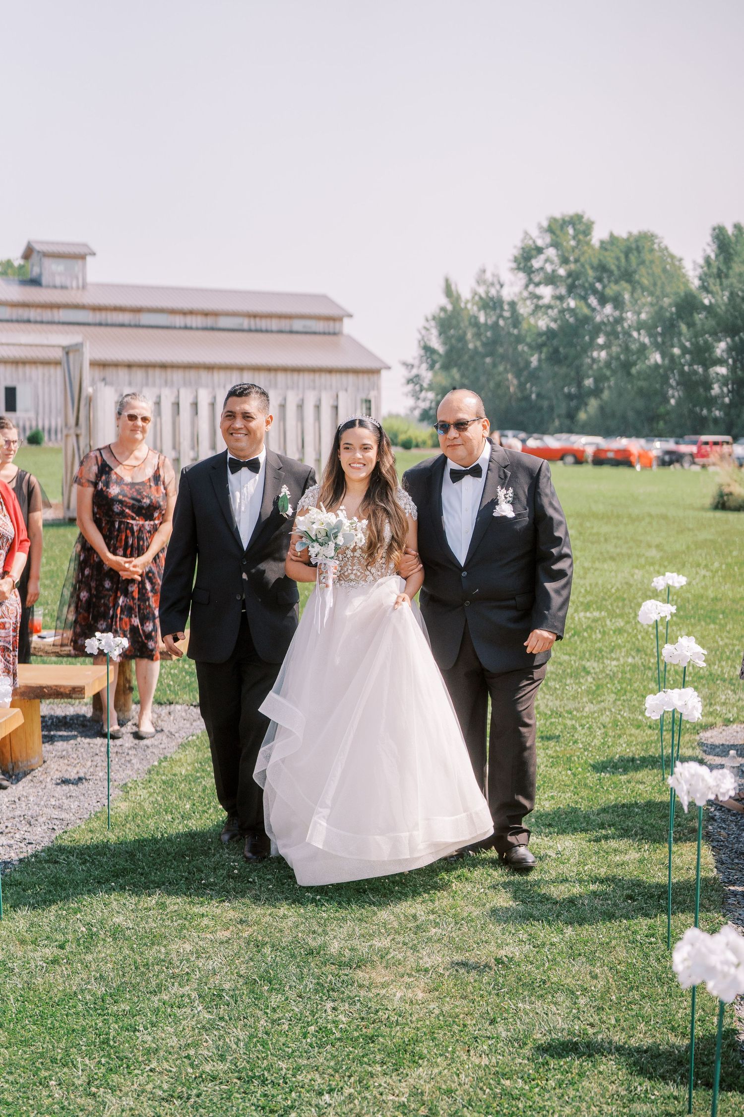 Outdoor wedding ceremony on a lush green lawn with white floral decorations lining the aisle.
