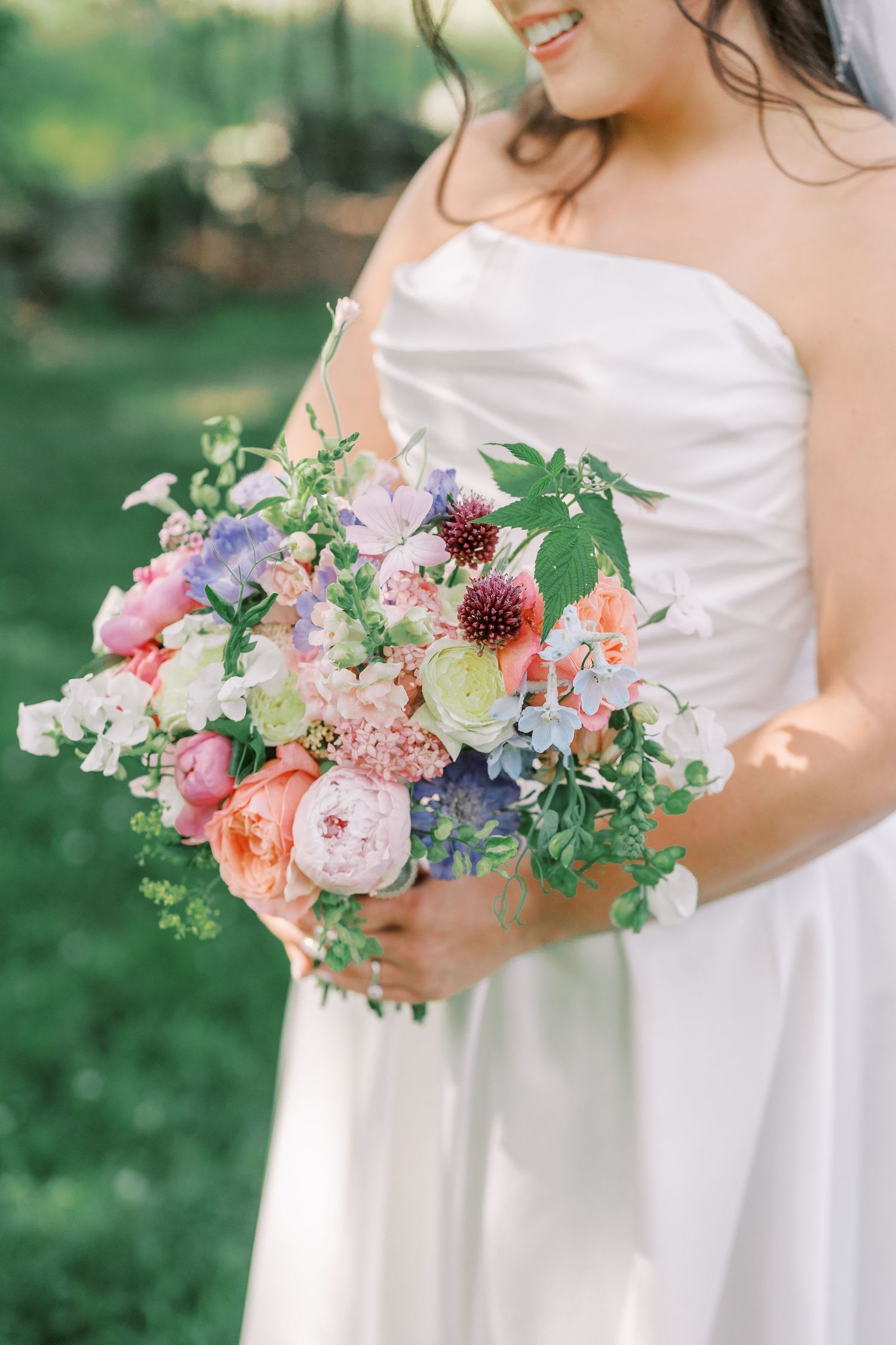 A romantic spring wedding bouquet features pink peonies, coral roses and purple blooms nestled with greenery.
