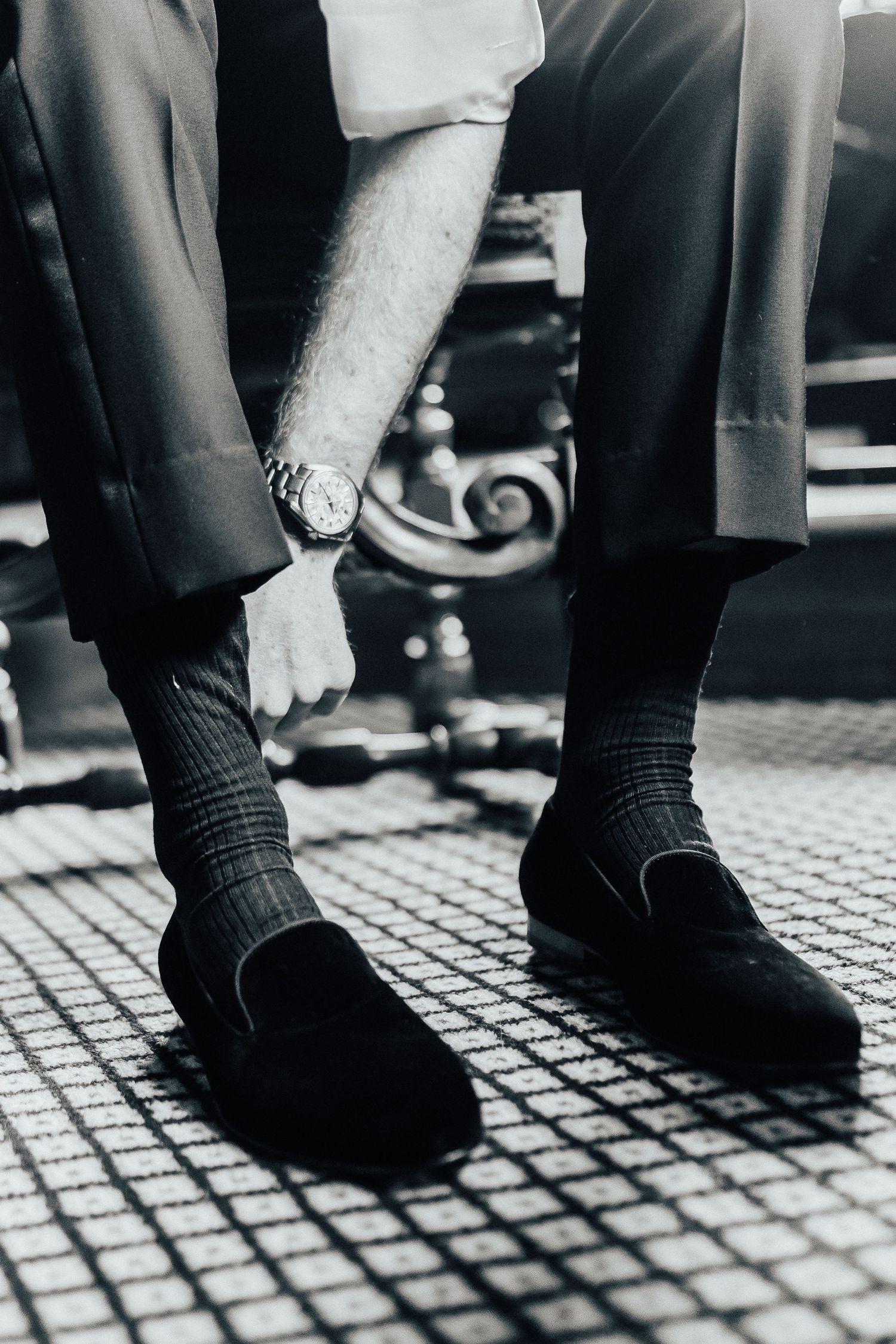 Close-up black and white image of a person wearing formal dress shoes and dark socks on a tiled floor.
