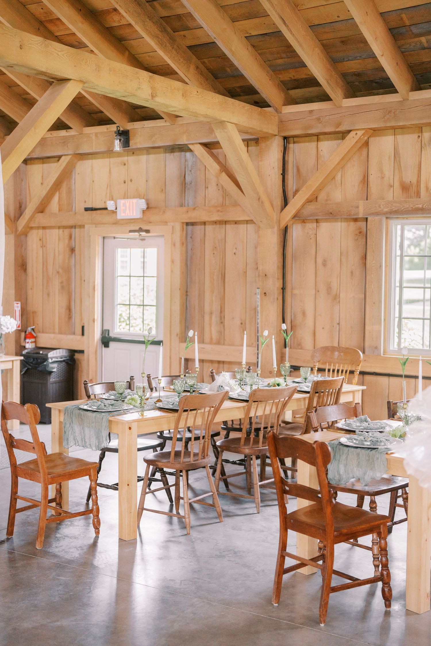 Rustic wooden barn interior set up as dining area with exposed beams, wooden tables and chairs under natural lighting.