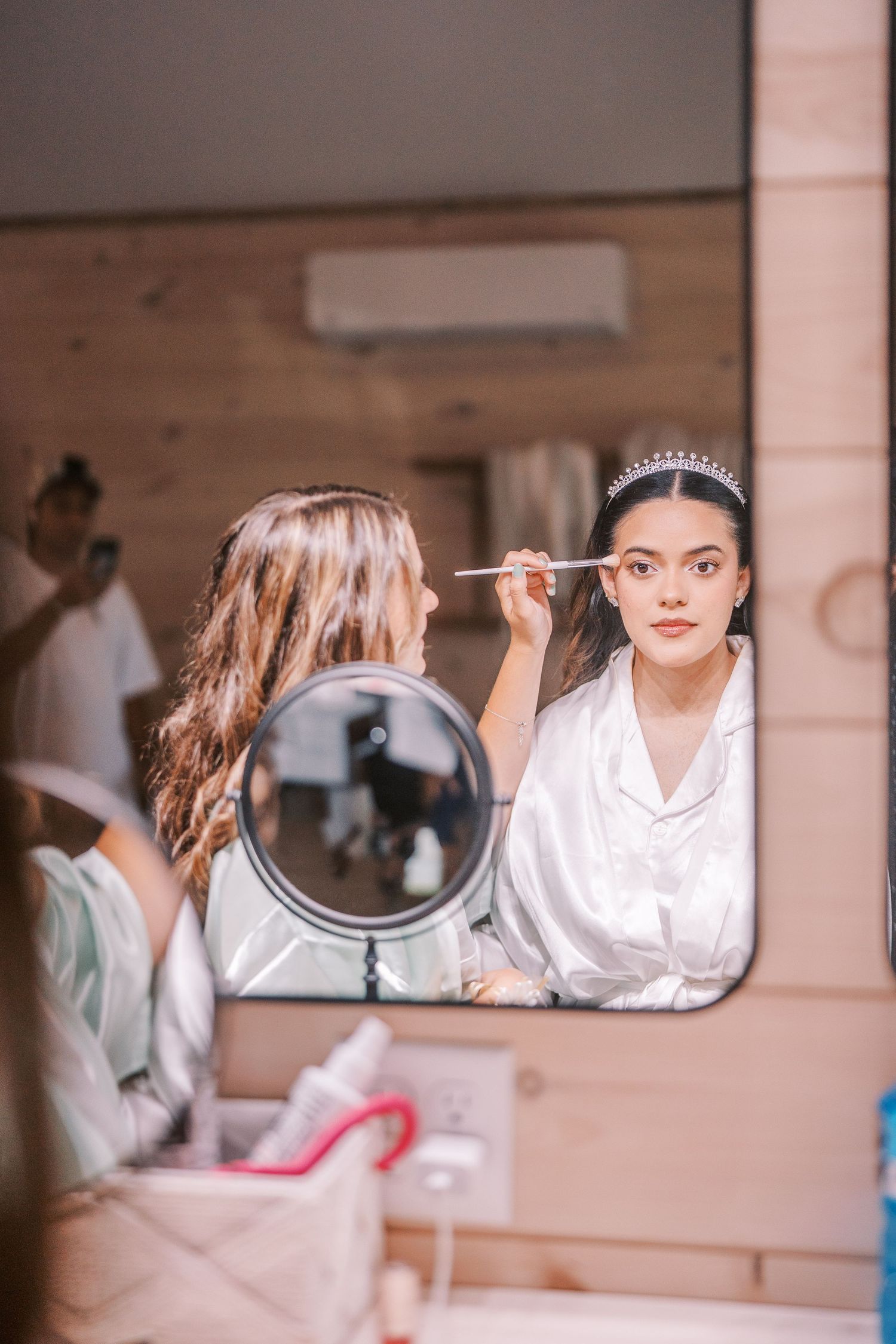 A sequence of mirror reflections shows a person in a white robe preparing for a formal event with elegant hair and makeup.