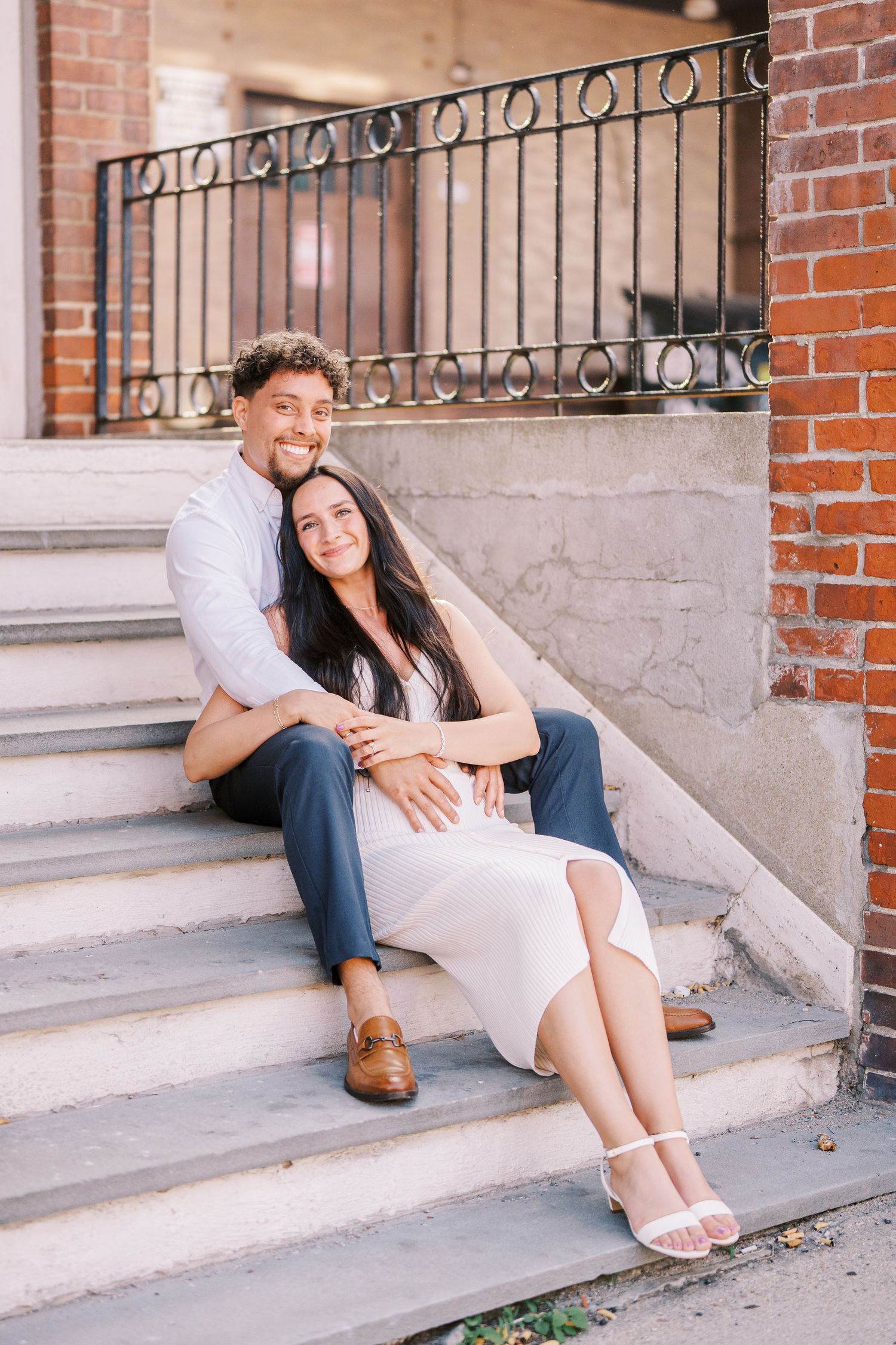 Couple sitting and posing playfully on brick building steps during a photo session.