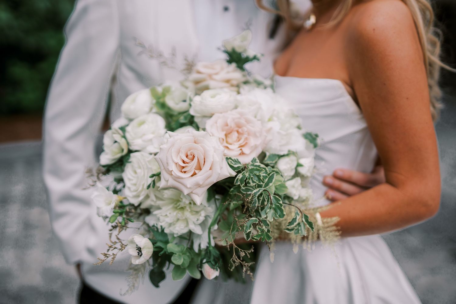 A romantic bridal bouquet featuring soft pink roses, white flowers, and delicate green foliage against a white dress.