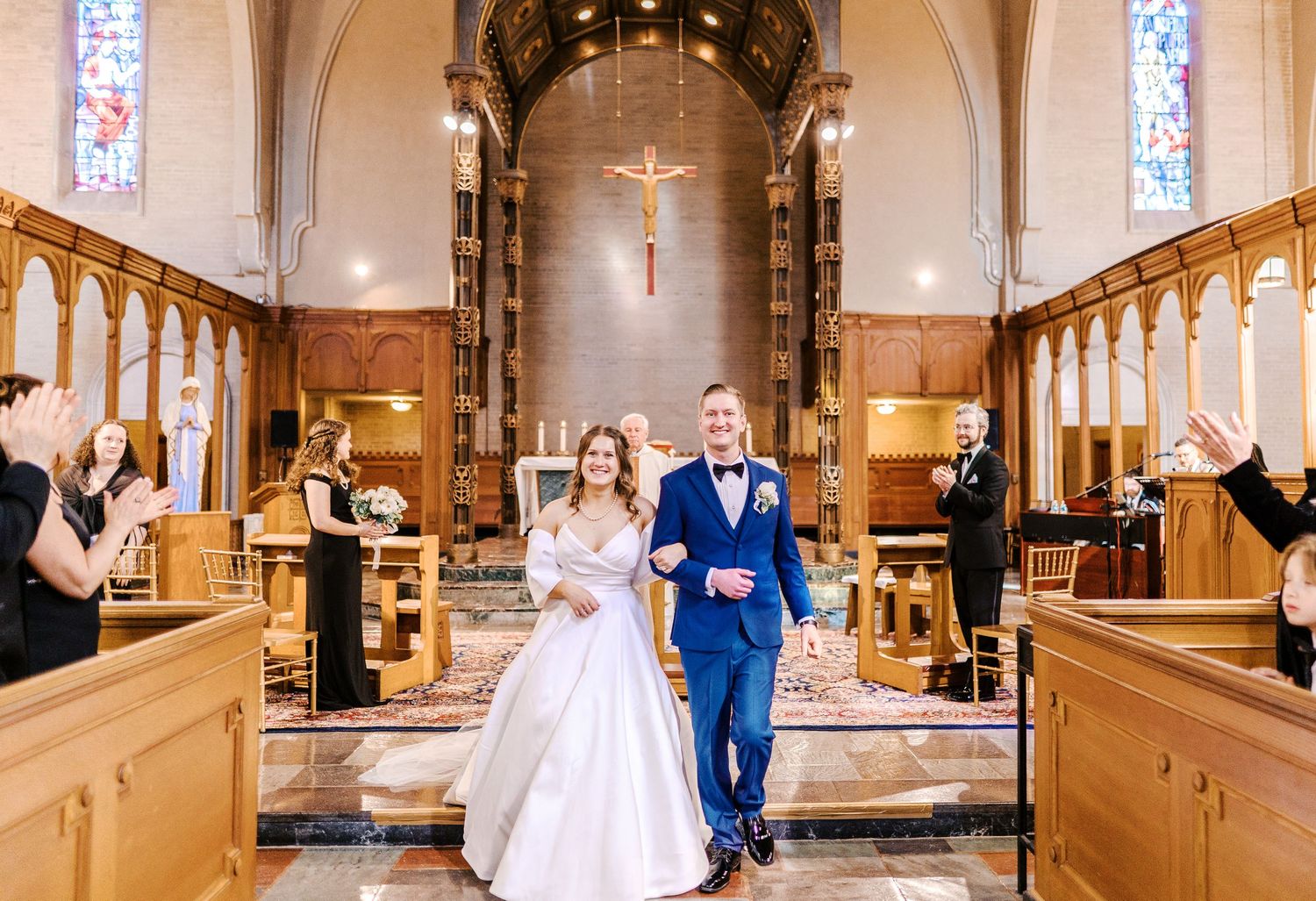 Wedding couple shares a joyful celebratory dance in the ornate church aisle with stained glass windows and wooden pews.