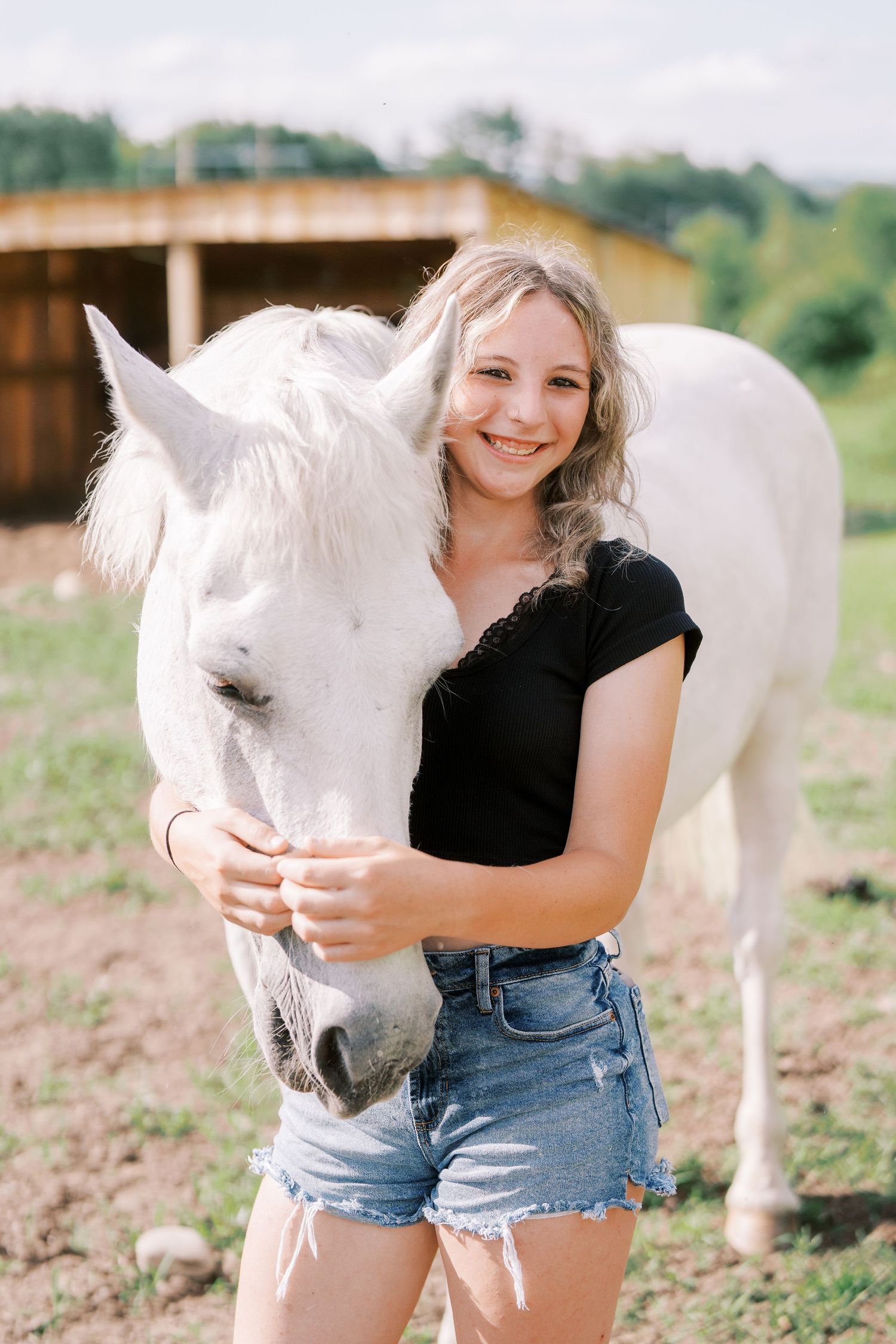 A series of candid photos featuring someone in denim shorts posing with a white horse in a sunny outdoor field.