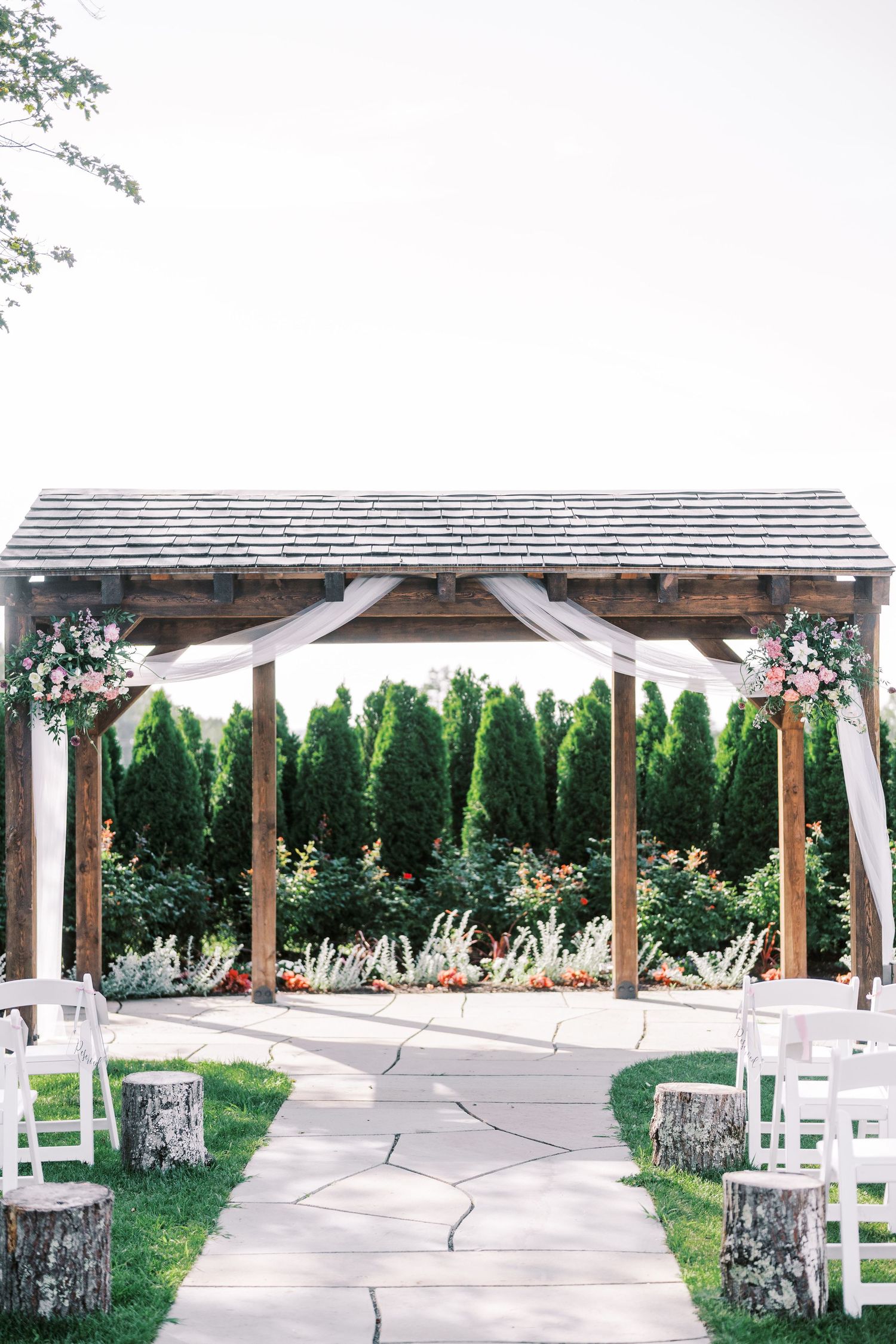 Rustic wooden wedding arbor decorated with white fabric and floral arrangements along a stone pathway.