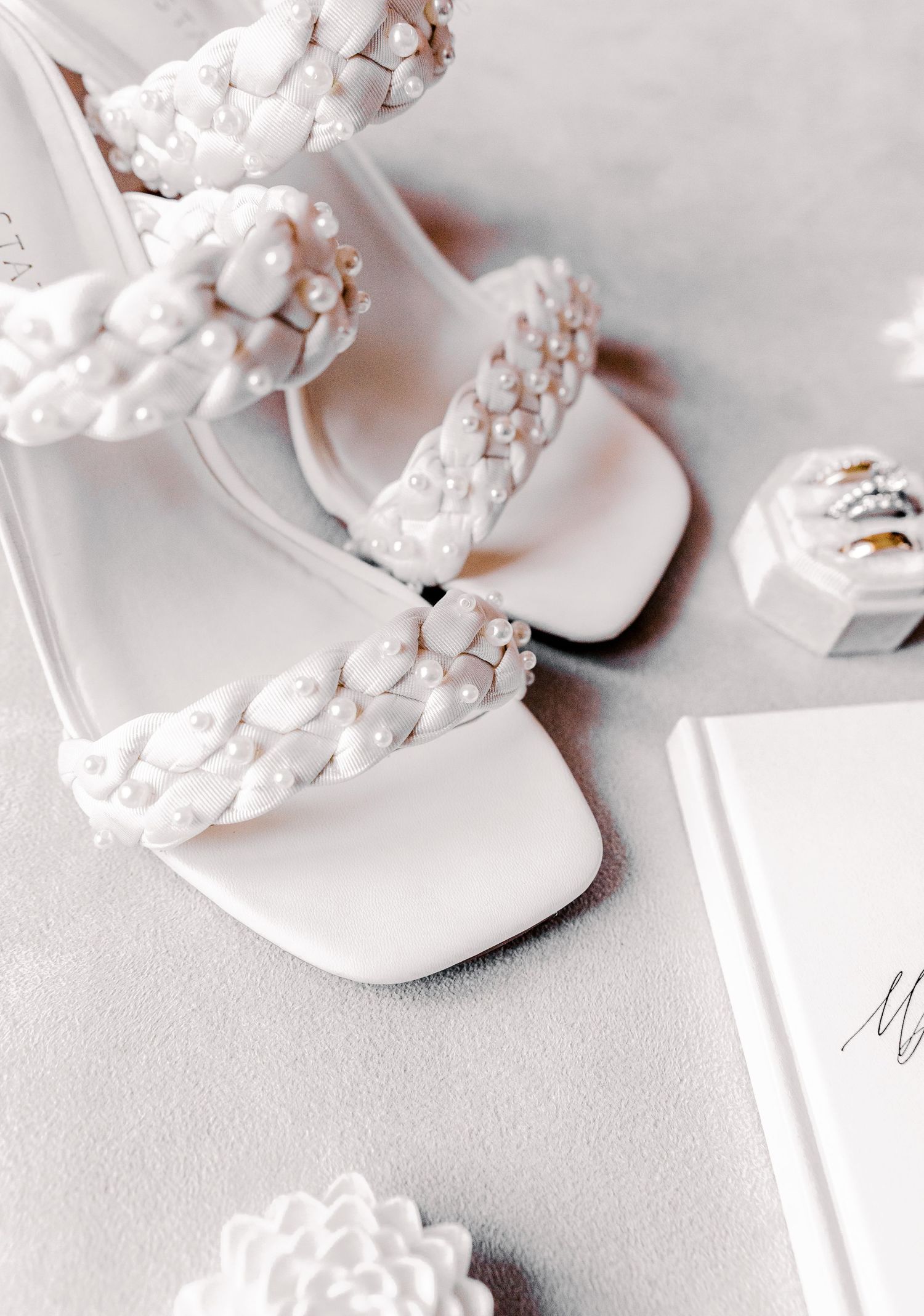 Close-up view of delicate white bridal flip flops with pearl embellishments on a light gray surface.