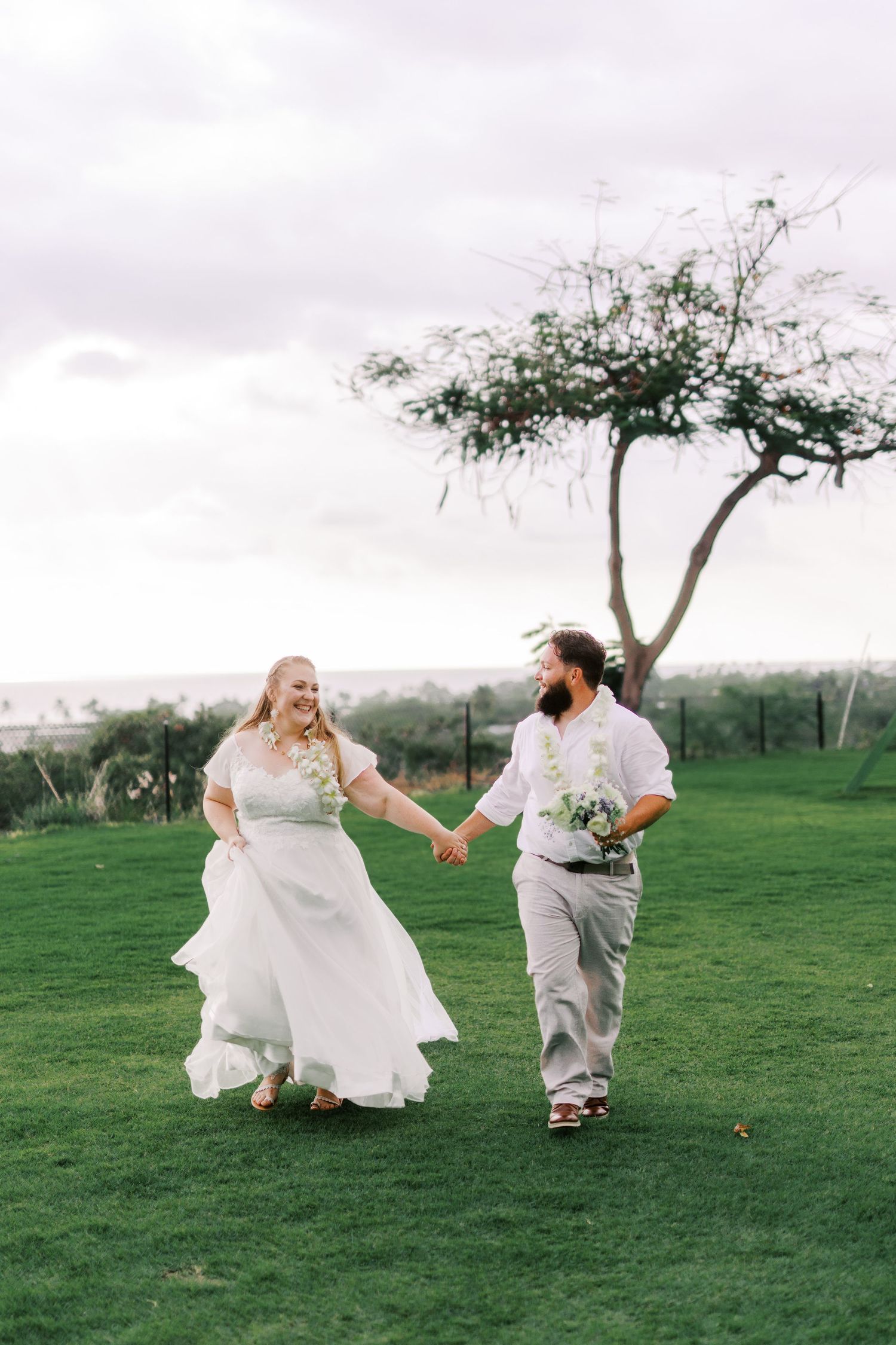 A joyful moment of newlyweds holding hands while walking across a green lawn with scenic overlook.