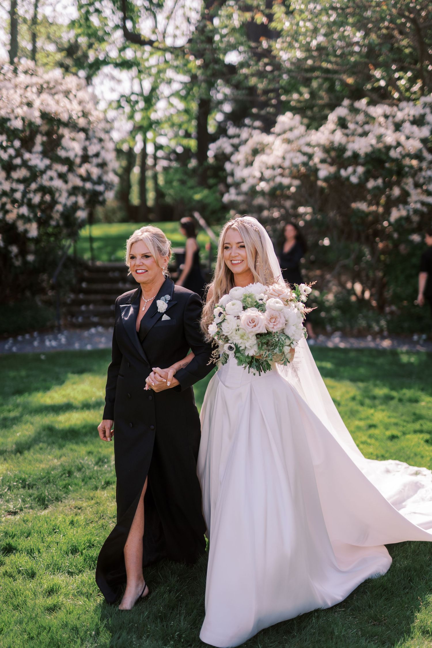Joyful wedding couple poses in front of blooming cherry blossom trees on a sunny spring day.