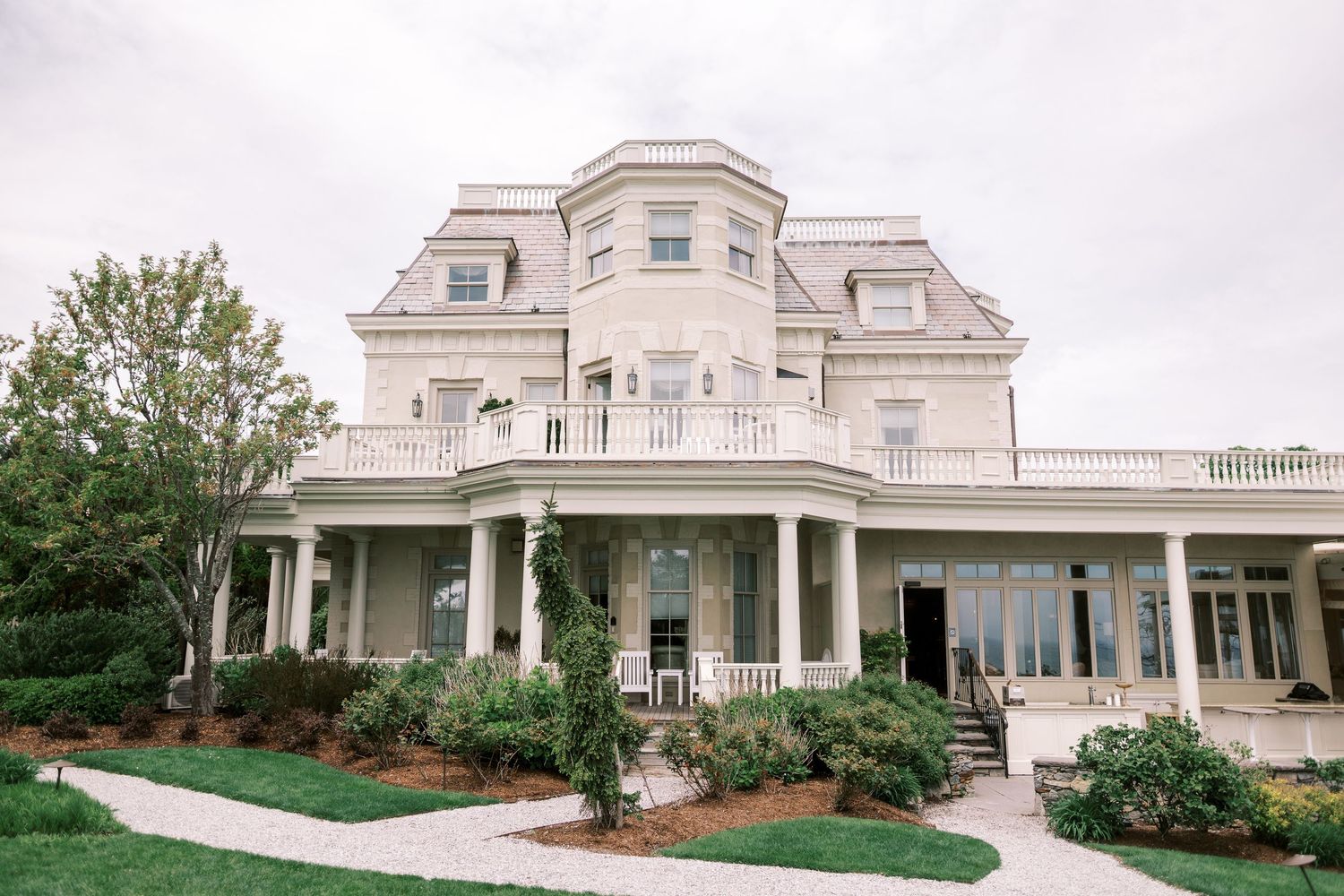 Elegant white mansion with wraparound porch and classical architecture features landscaped gardens and ornate details.