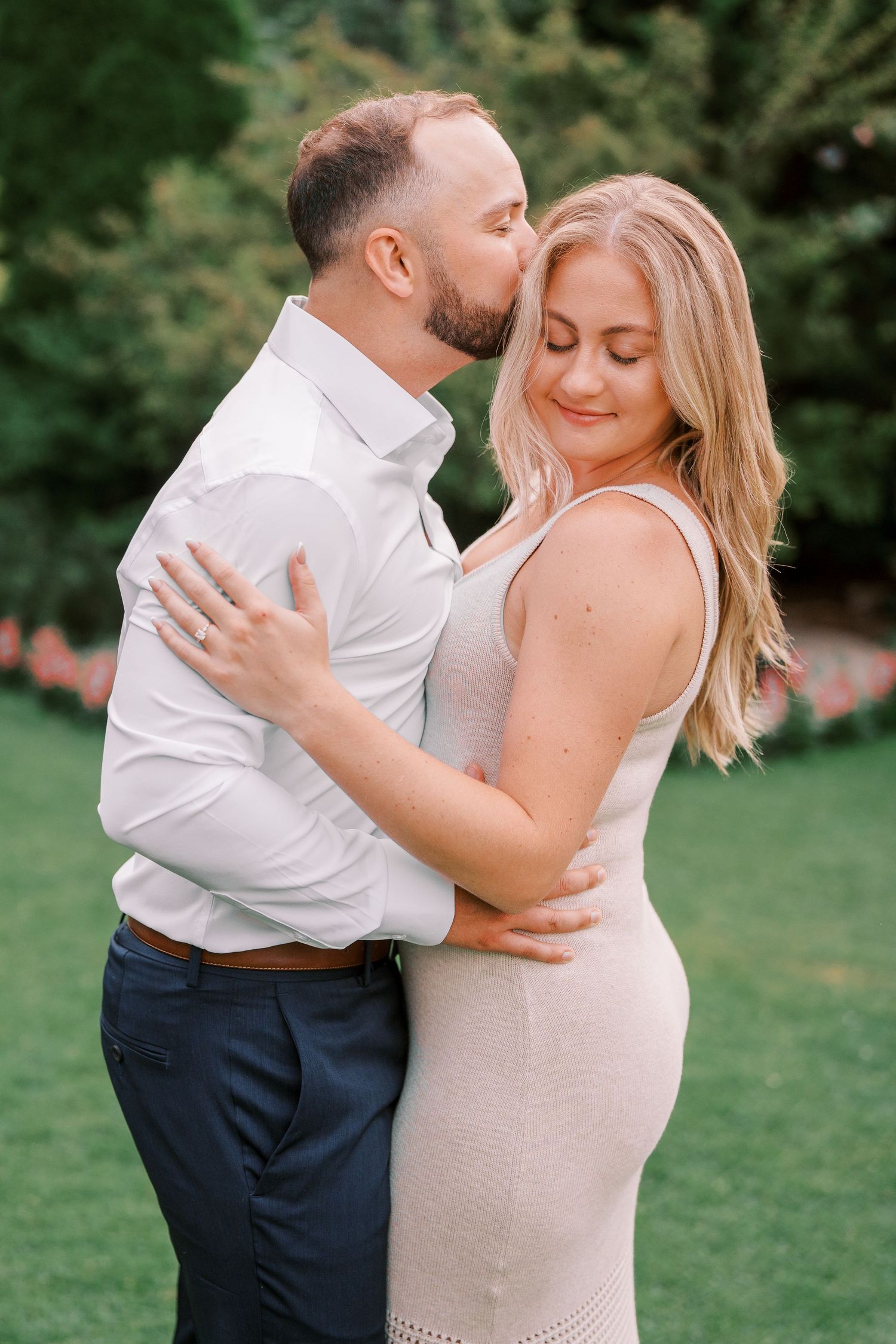 Romantic couple embrace in garden setting wearing white and beige attire.