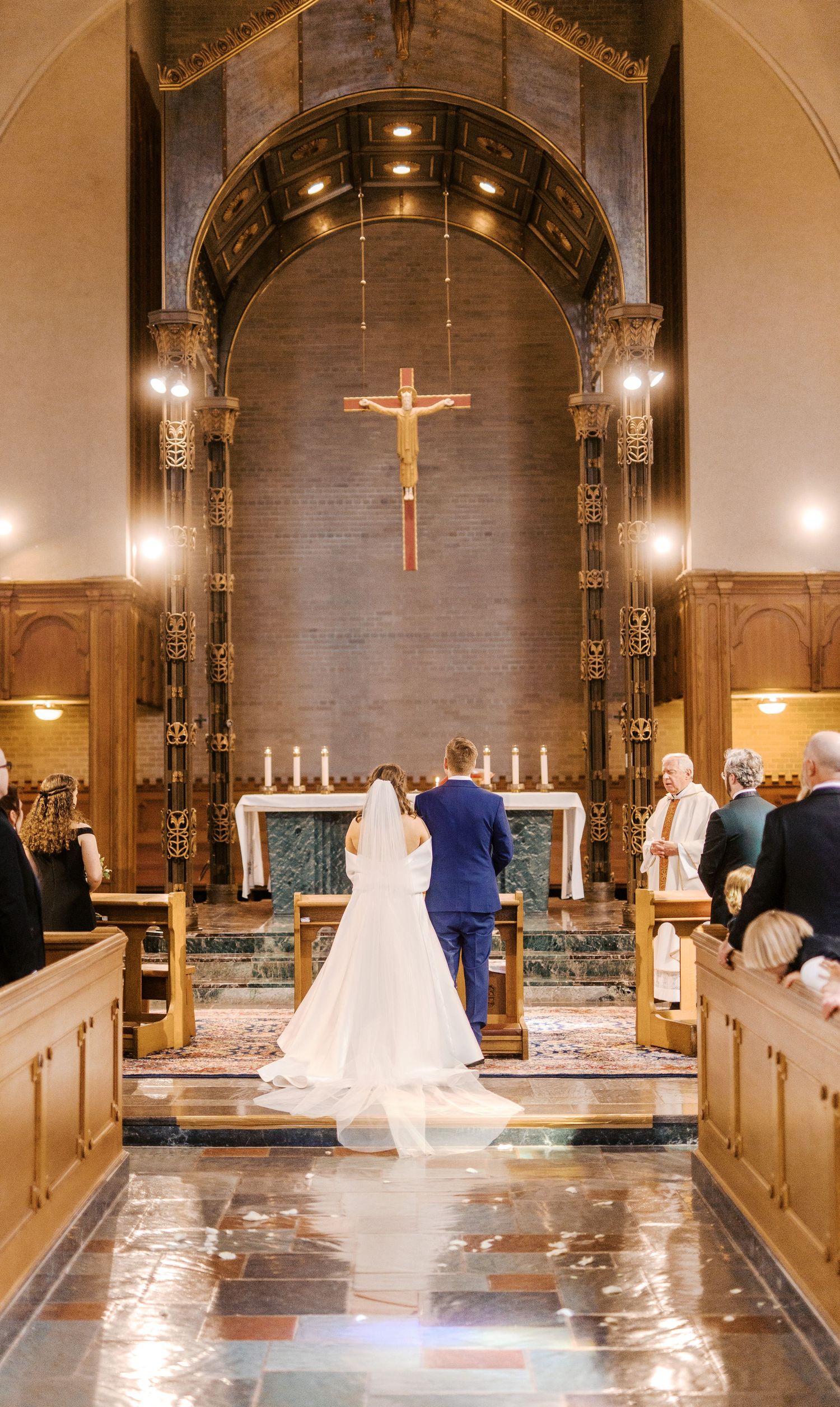 Bride and groom standing at altar during Catholic church wedding ceremony with crucifix and candles.