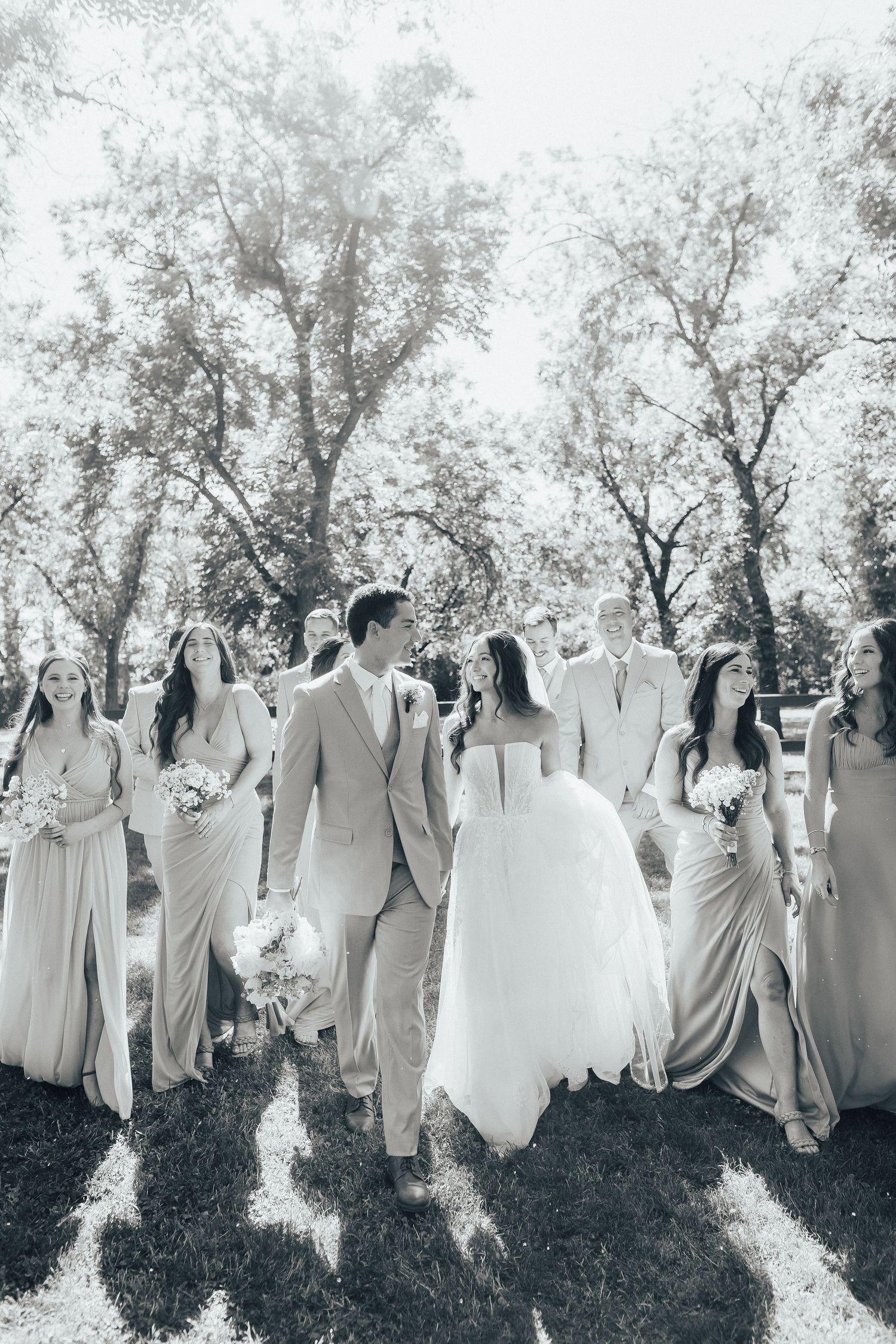 A black and white photo of a wedding party walking together outdoors with bridesmaids in flowing dresses.