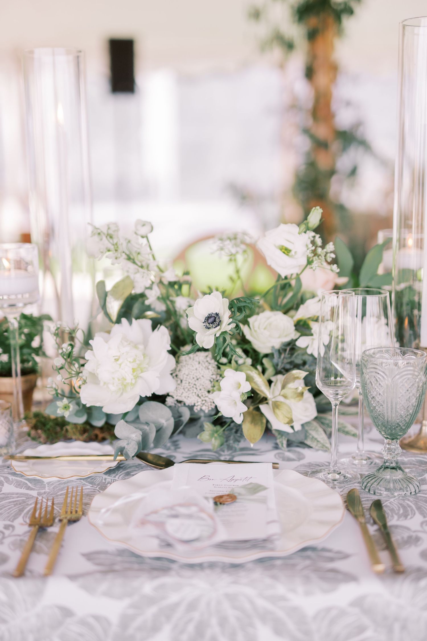 Elegant wedding table centerpiece with white flowers, eucalyptus greens, and crystal glassware on light linens.