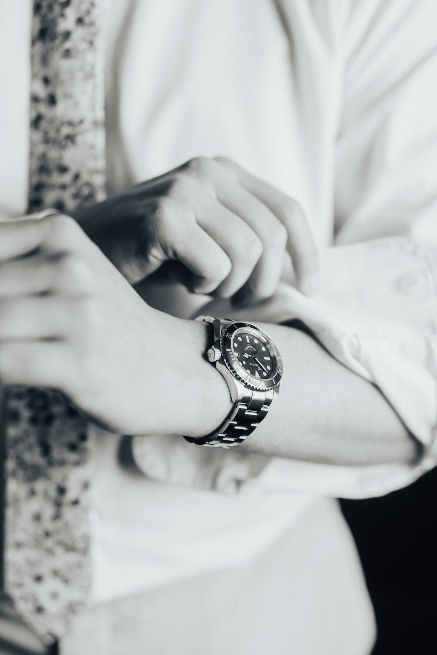 Close-up of hands adjusting a silver luxury watch against white formal attire.