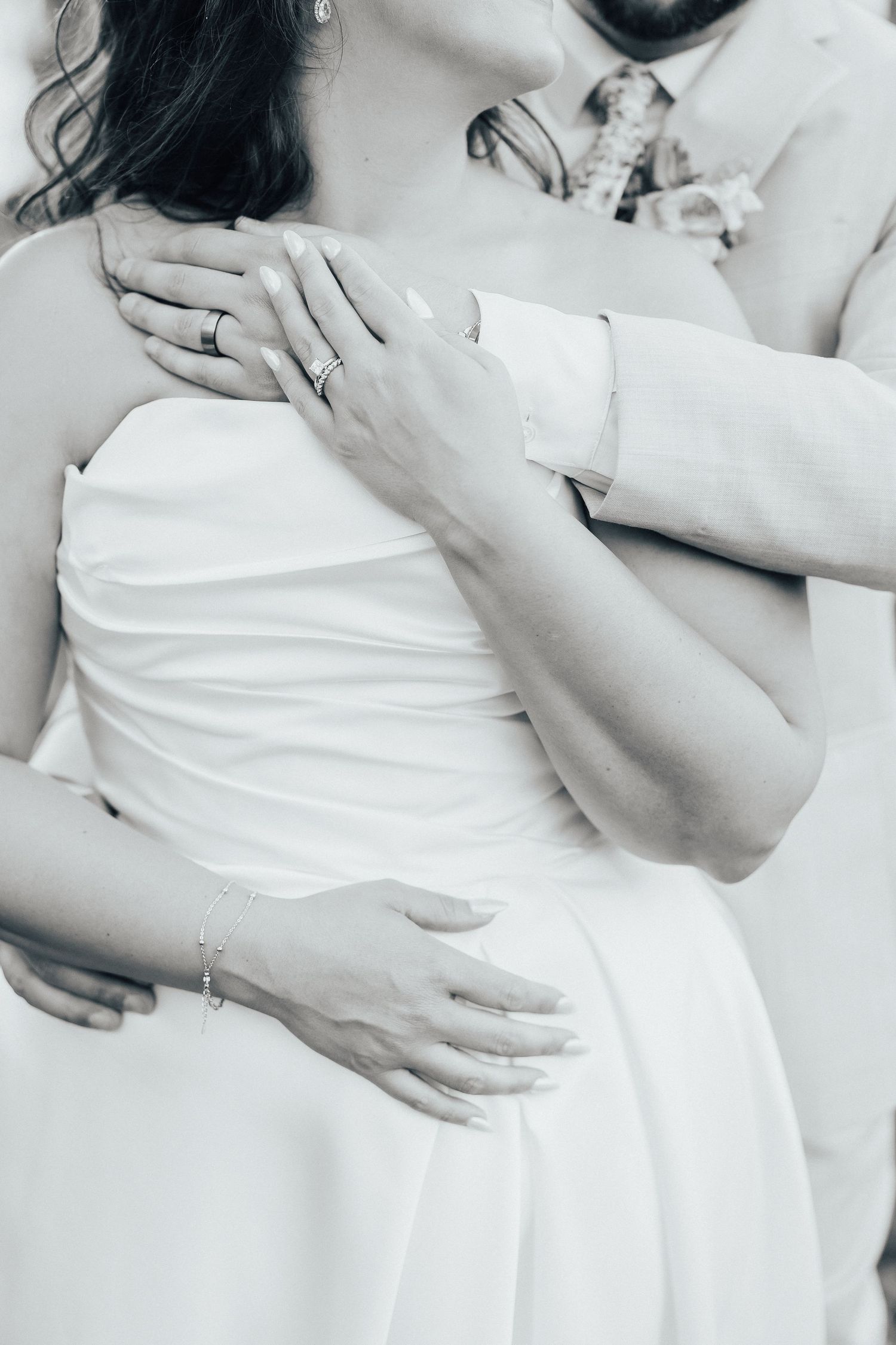 Close-up black and white photo of hands embracing in formal wedding attire.