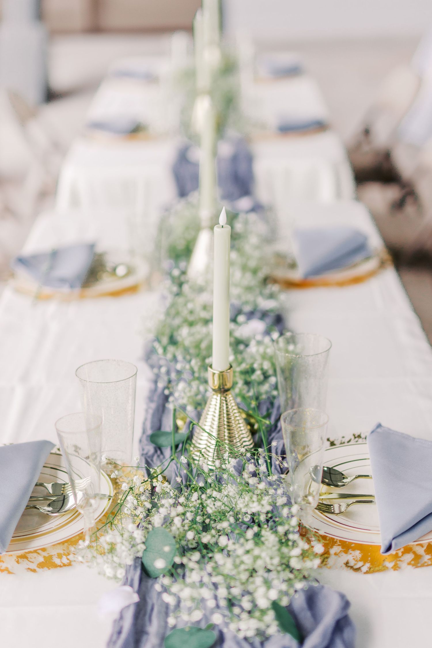 An elegant wedding table setting with blue napkins and delicate baby's breath centerpieces.