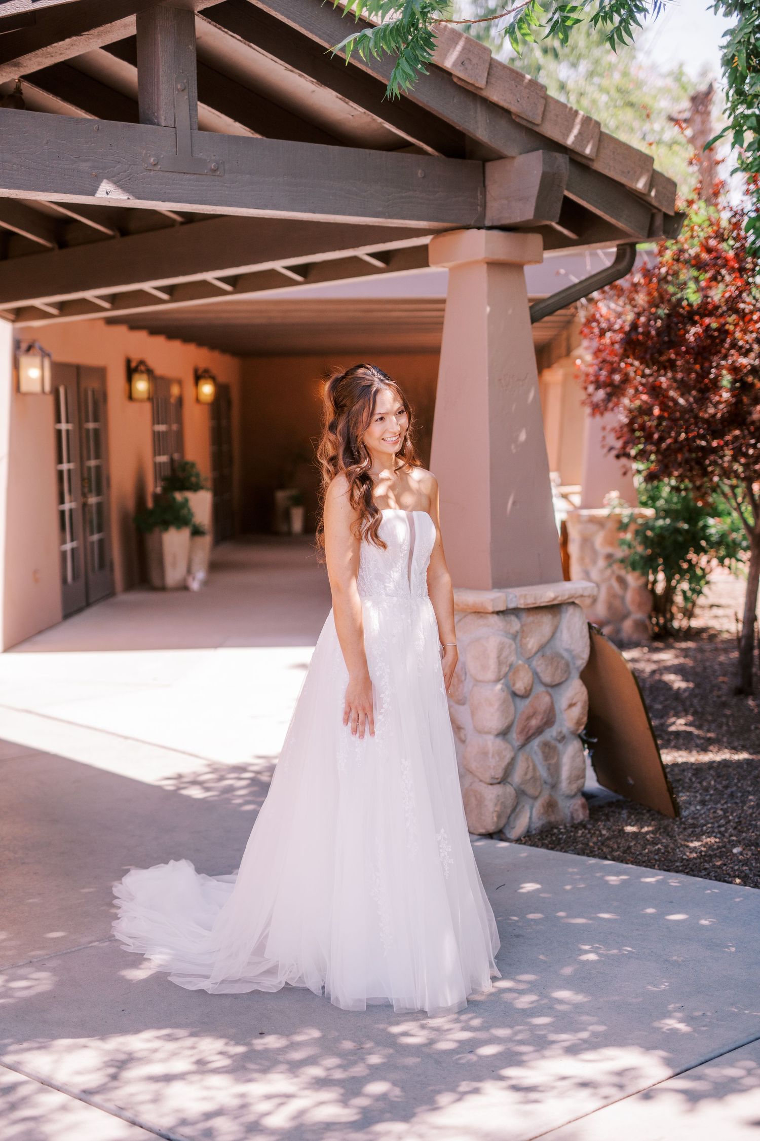 A flowing white wedding dress swirls gracefully in the sunlight under a rustic wooden beam porch.