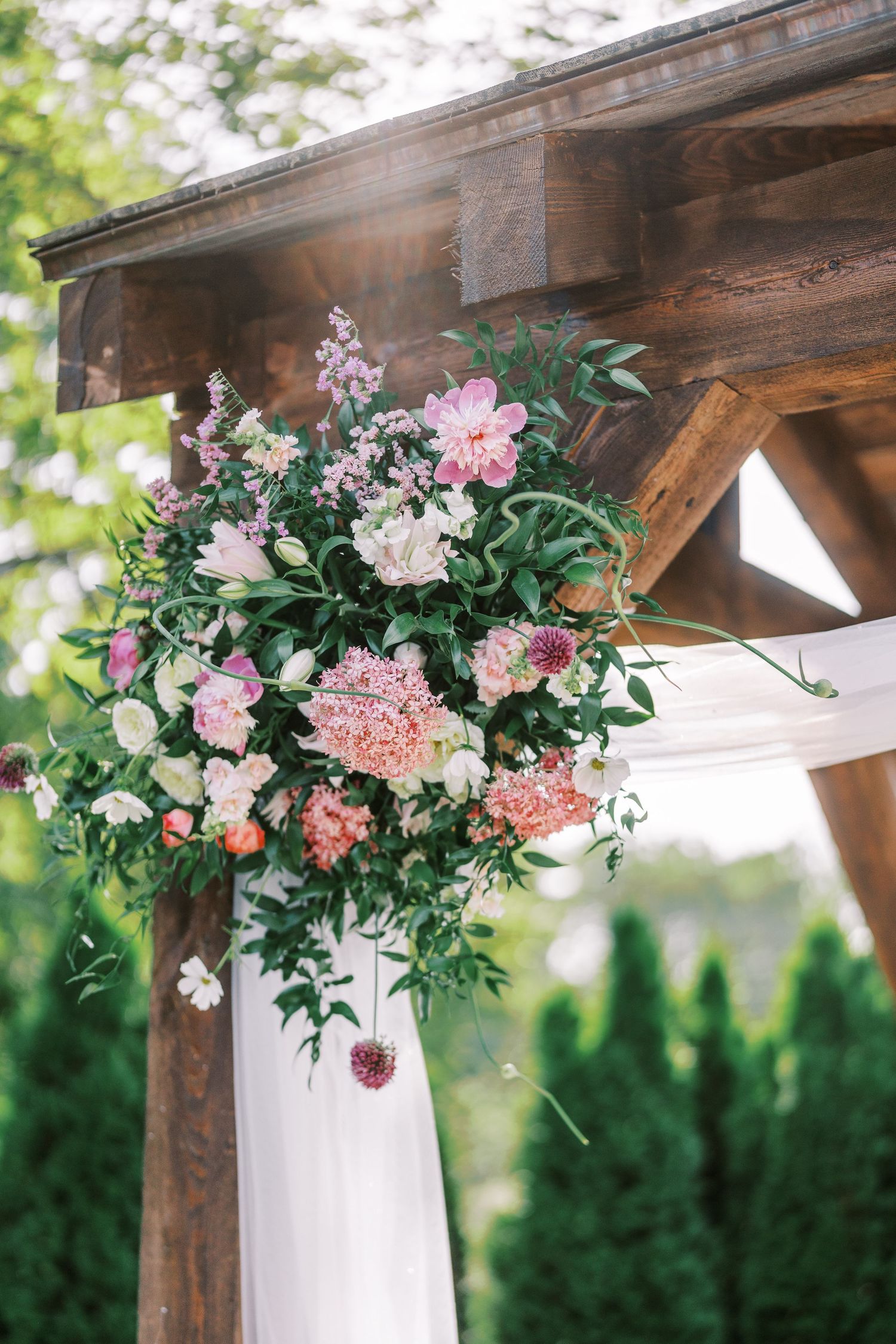 Stunning floral arrangement with pink flowers and greenery adorning wooden wedding arch.