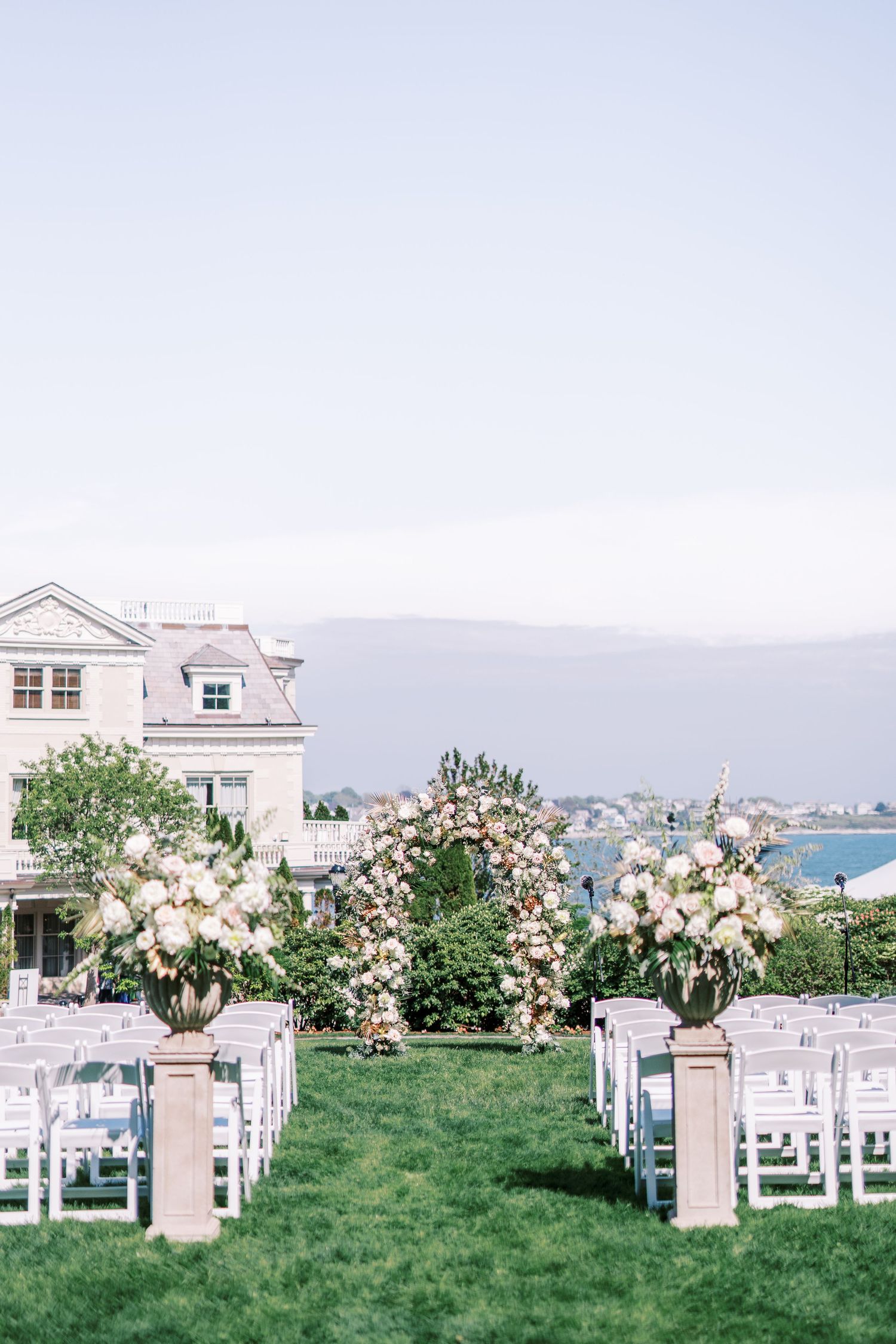White floral arrangements line the outdoor ceremony aisle with mountain views and white chairs on a grassy lawn.