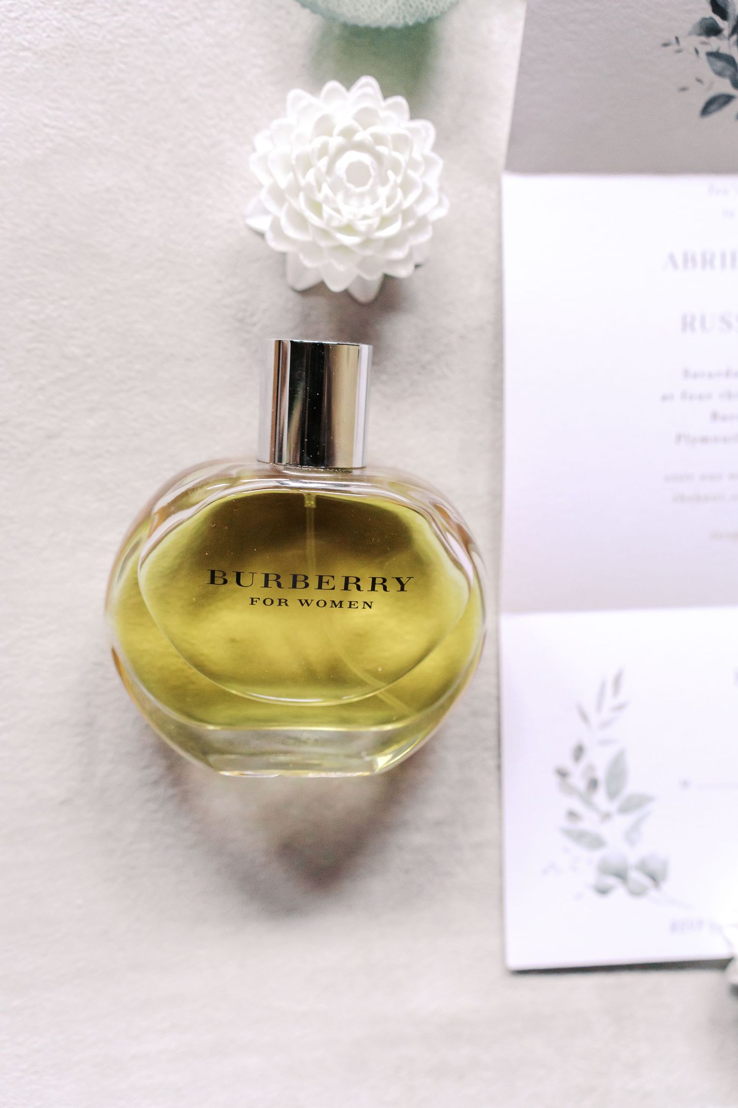 Burberry perfume bottle with white floral topper displayed next to wedding stationery.