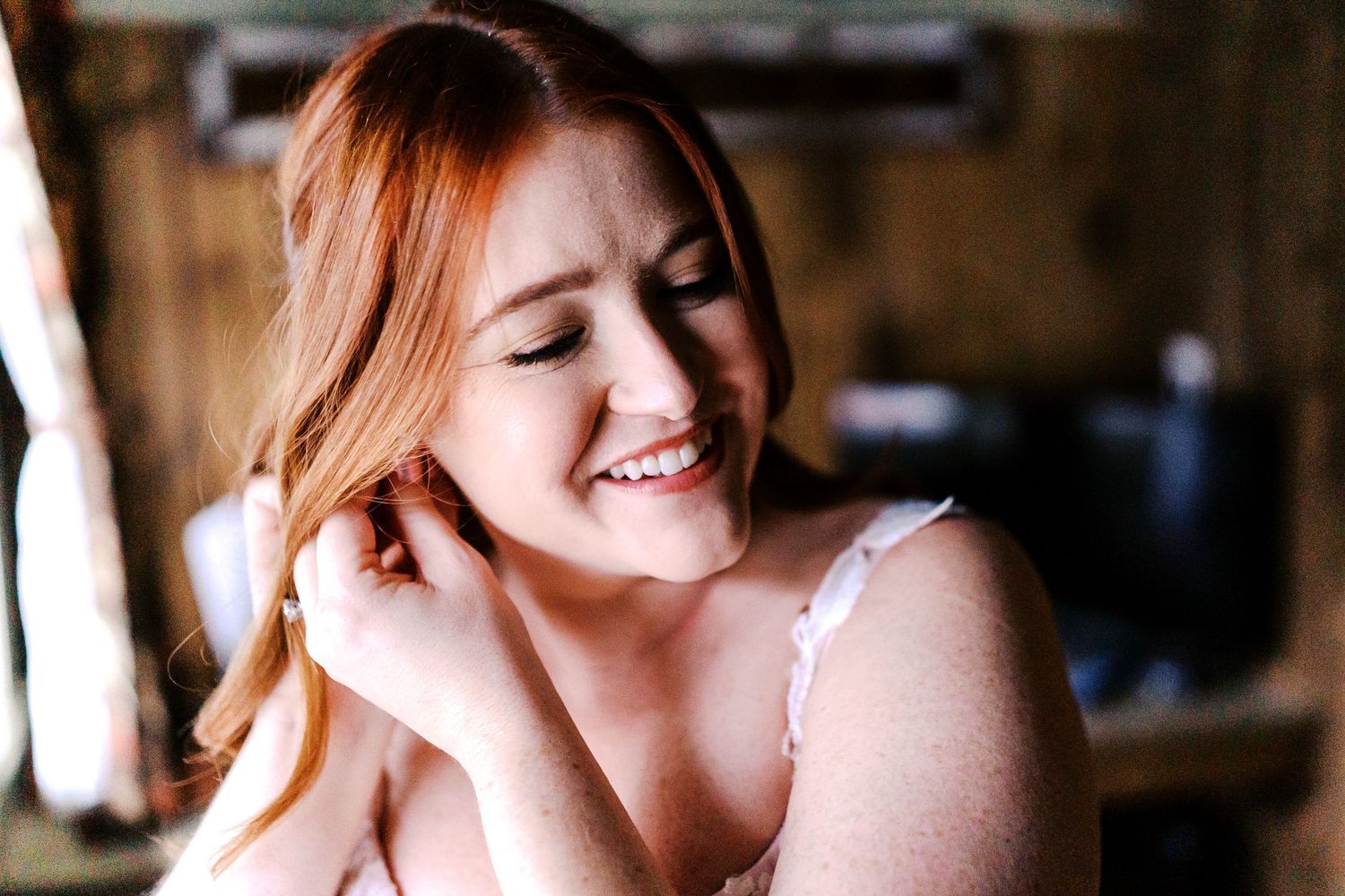 A person with red hair smiles warmly while seated in a casual indoor setting with soft natural lighting.