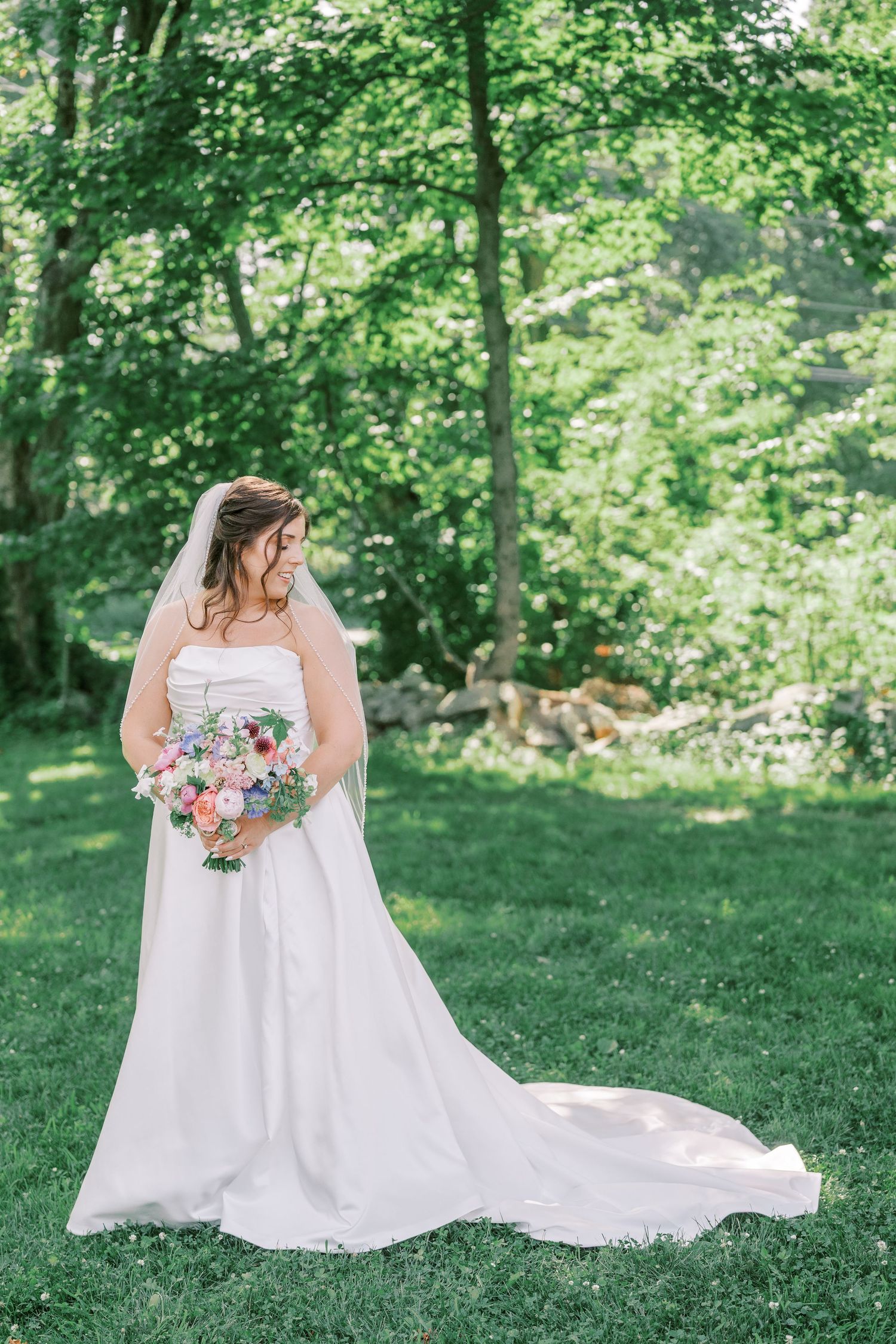 A flowing white wedding gown with a long train spreads elegantly across green grass in an outdoor setting.