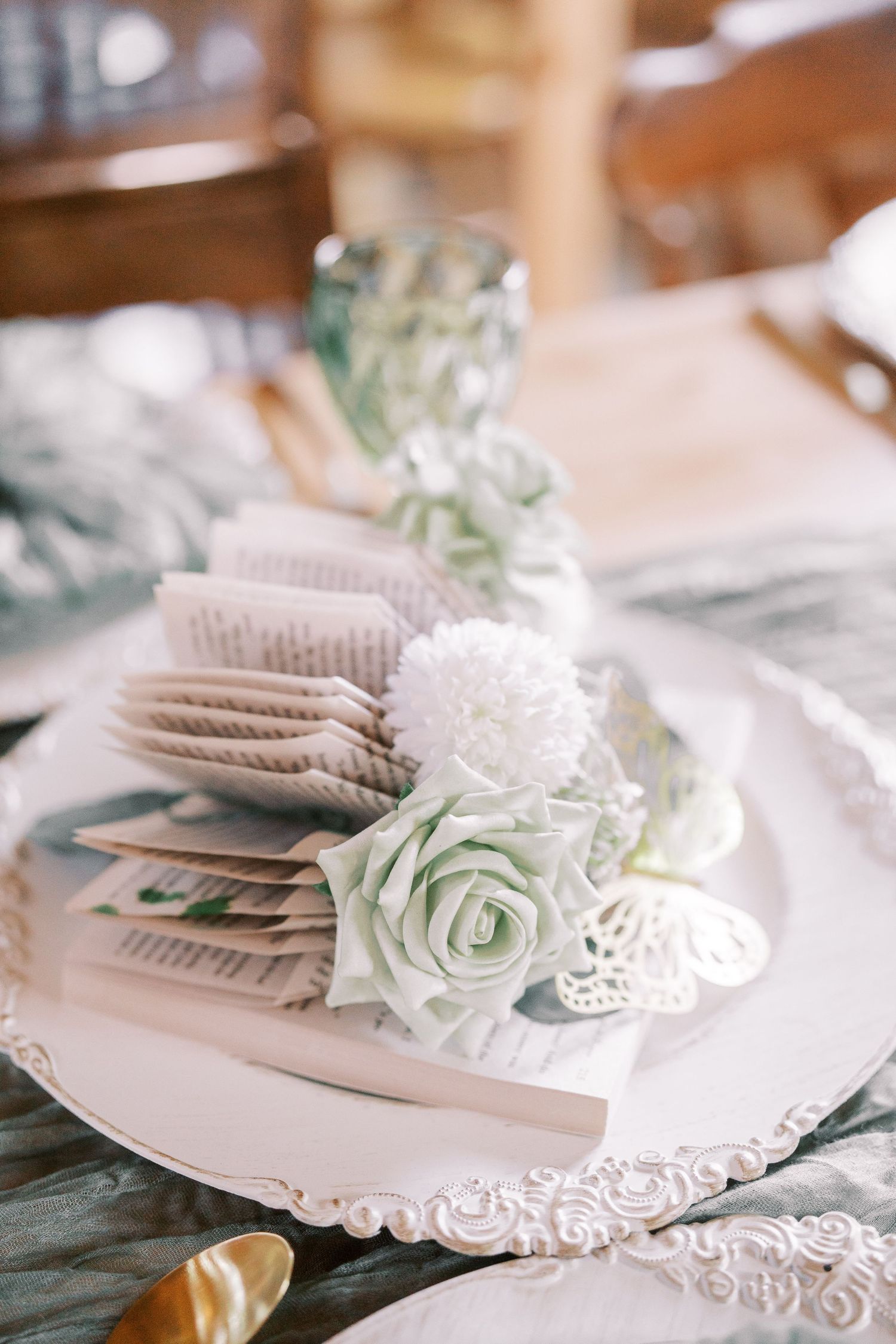 Elegant place setting with pale green roses and white doilies on ornate plate against soft pastel background.