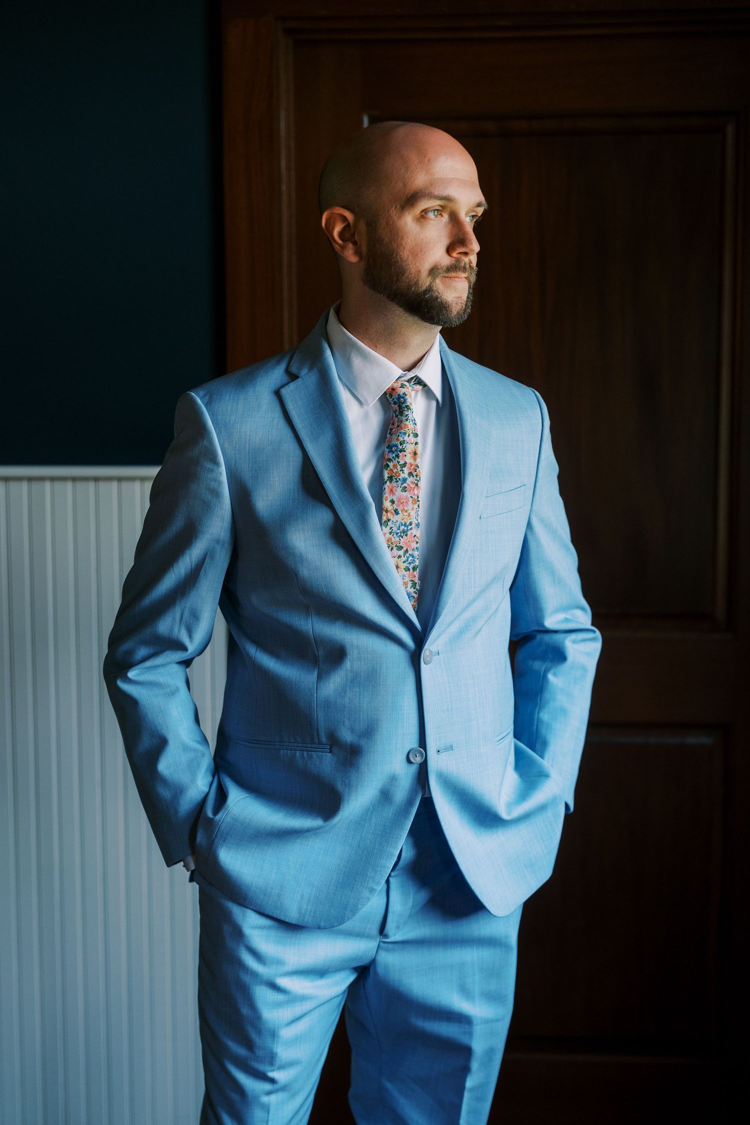 Formal light blue suit with floral tie photographed in dramatic lighting.