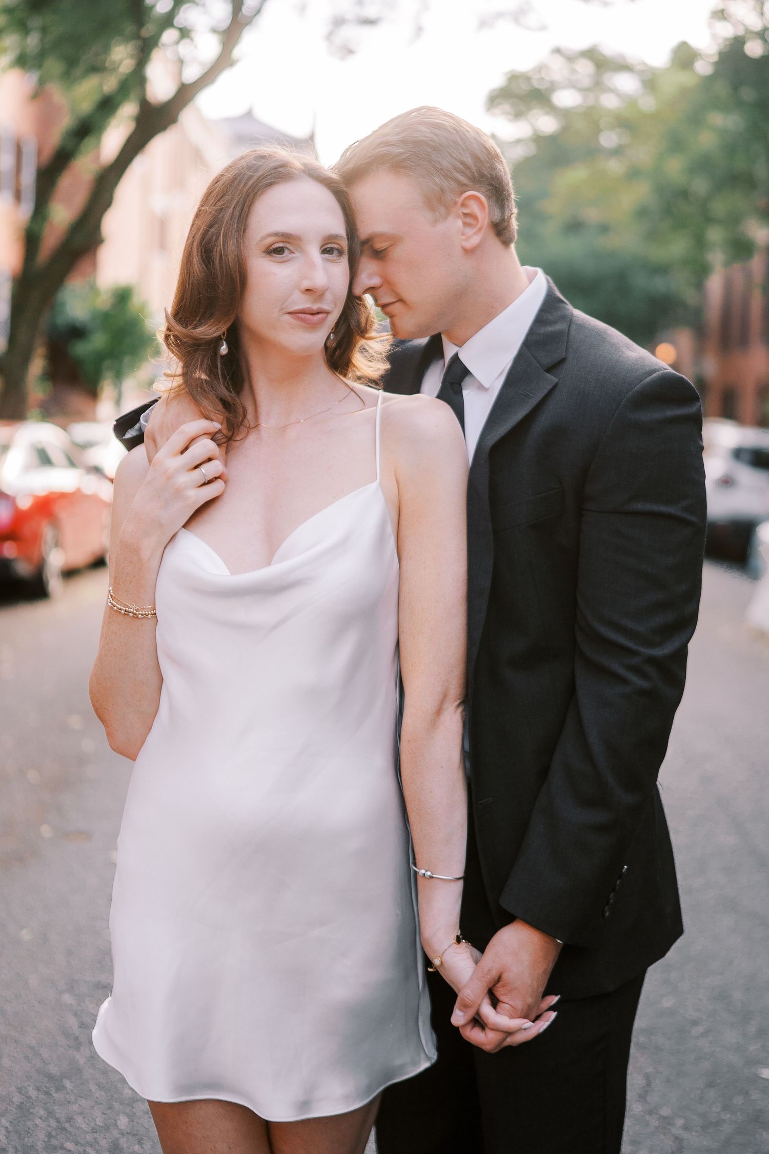 Romantic couple in formal attire share intimate moments while walking on a cobblestone street during golden hour.