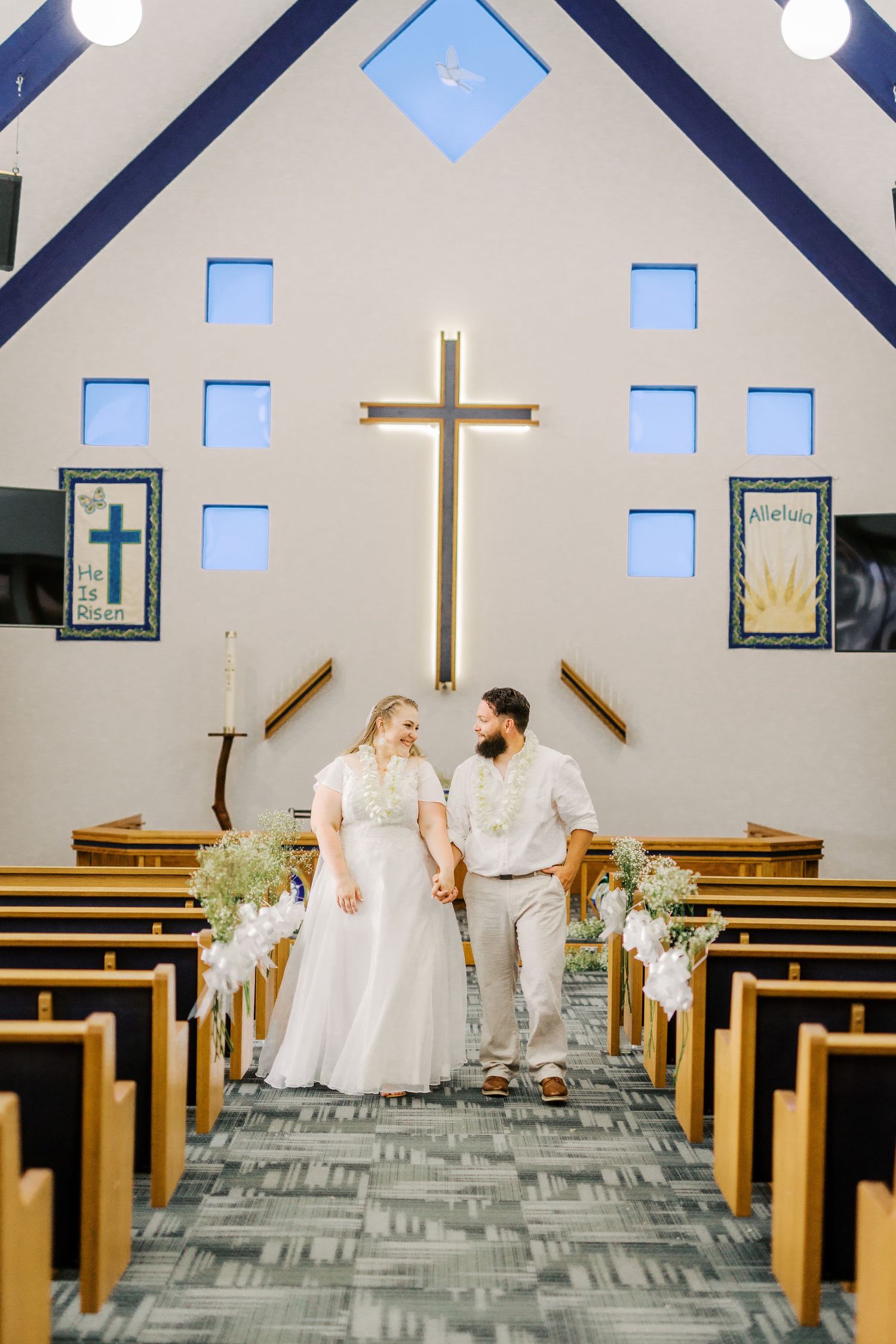 A couple stands in a modern church sanctuary with blue windows and a large illuminated cross.