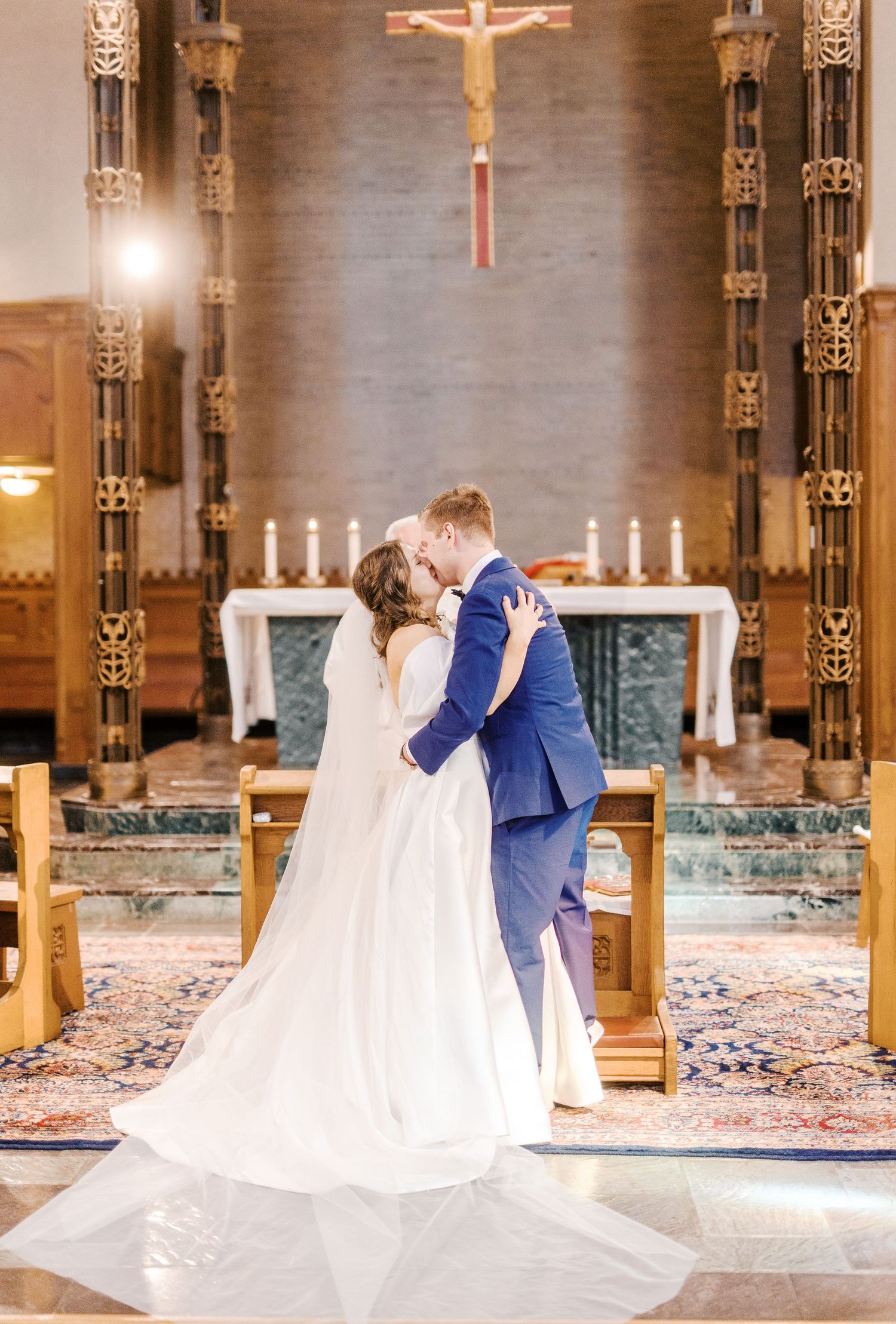 A romantic wedding ceremony in a church with ornate pillars, candles and a crucifix altar in the background.