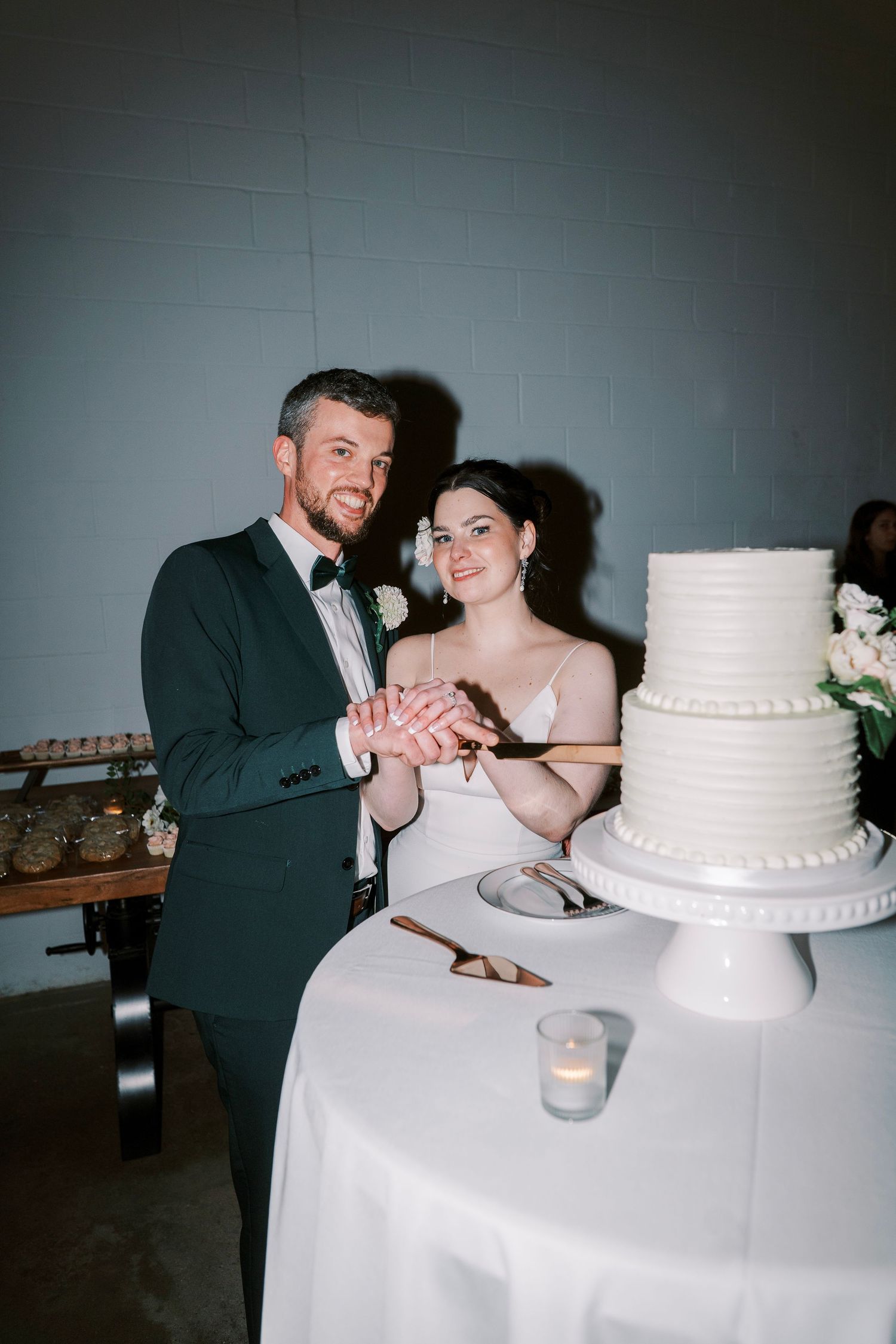 A newlywed couple cuts their two-tier white wedding cake together at their reception.