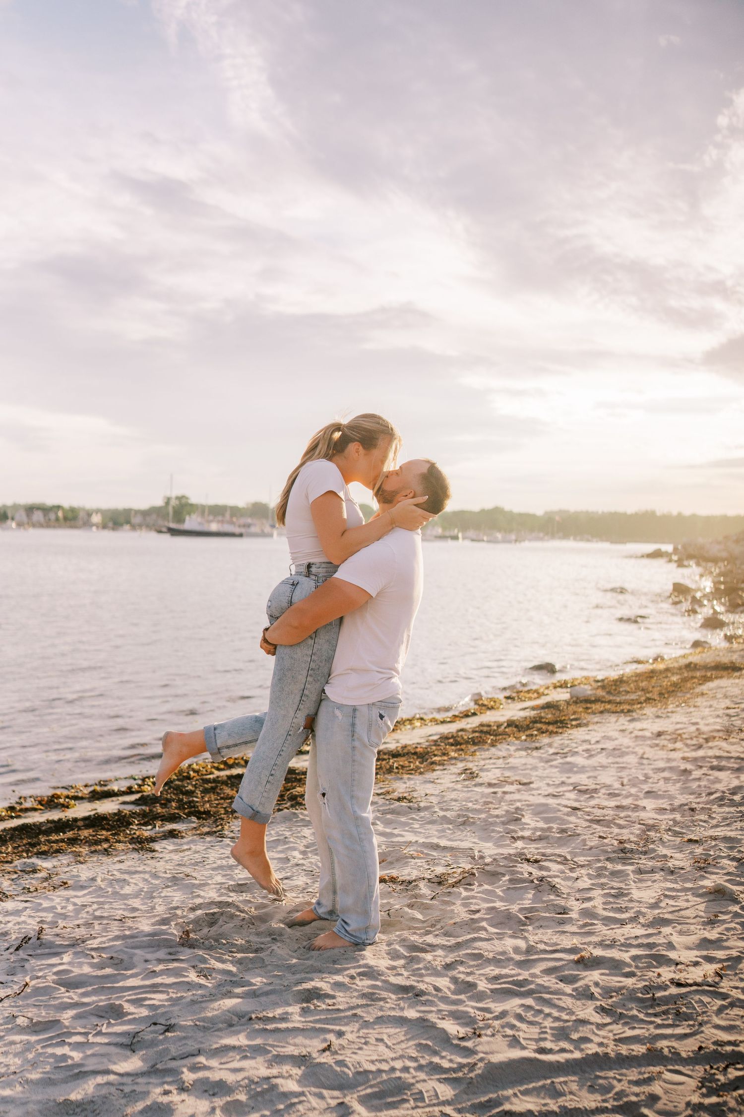 Romantic sunset embrace on sandy beach with coastline in background.